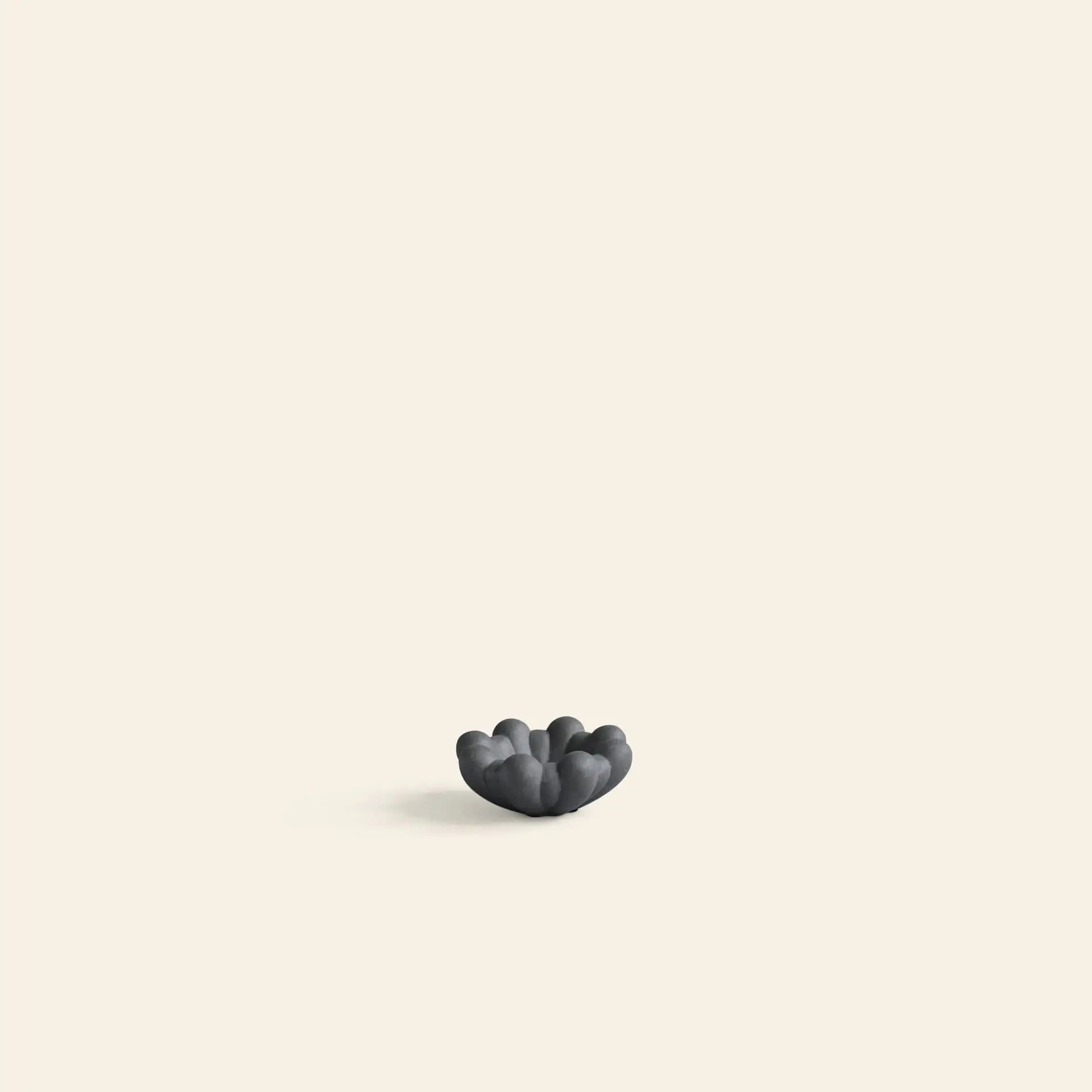 A small, dark, organic-shaped 101 Copenhagen Bloom Tray, Mini by 101 Copenhagen sits at the center-bottom of a plain light beige background with ample negative space above.
