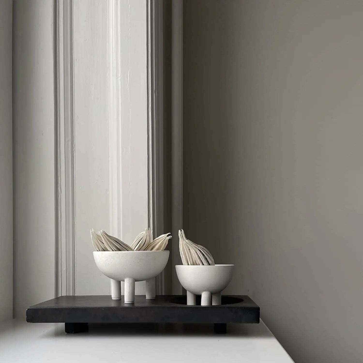 Two modern white 101 Copenhagen Duck Bowl Minis with vertical legs, each holding folded napkins, sit on a black rectangular tray against a minimalist light gray wall—a striking home decor piece from 101 Copenhagen.