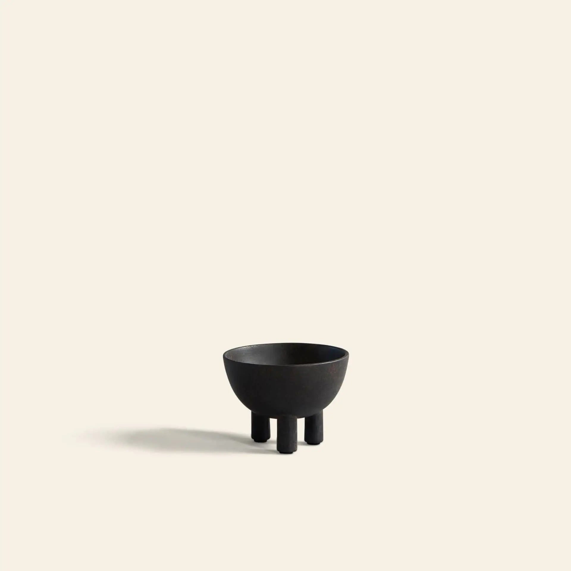 The 101 Copenhagen Duck Bowl, Mini by 101 Copenhagen is a small, matte black bowl with three short legs, centered on a light beige background and casting a soft shadow—an elegant addition to modern home decor.