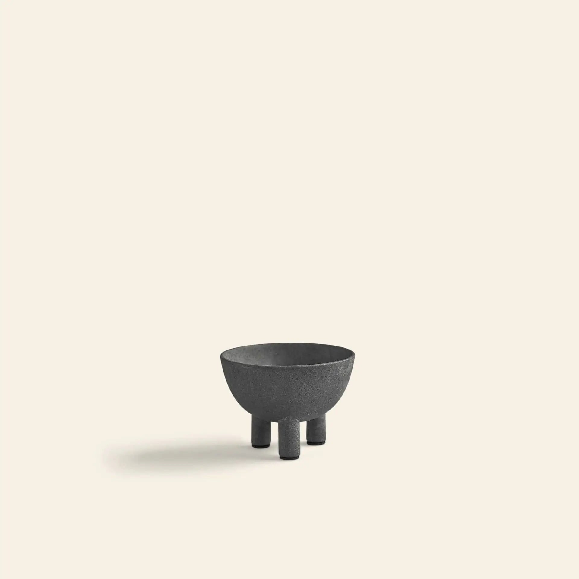 The 101 Copenhagen Duck Bowl, Mini by 101 Copenhagen is a small black round bowl with four short legs, shown on a light beige surface with a soft left shadow—a stylish, modern accent for your home decor.