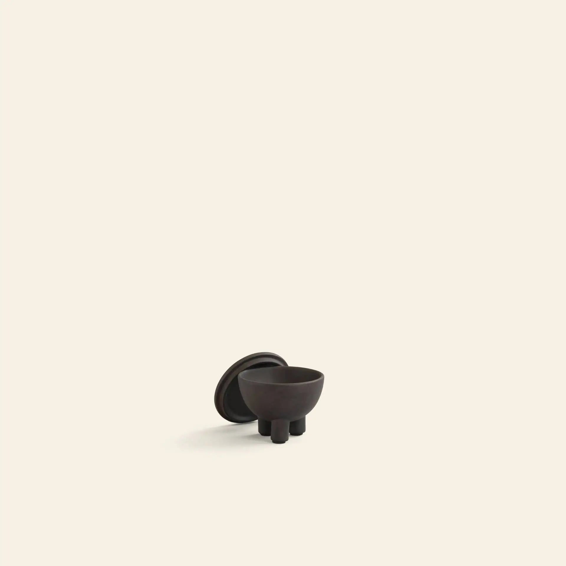 The 101 Copenhagen Duck Jar, Mini by 101 Copenhagen features a small, dark three-legged design with a matching round lid, sitting on a surface against a beige background—making it both a unique storage and decorative piece.
