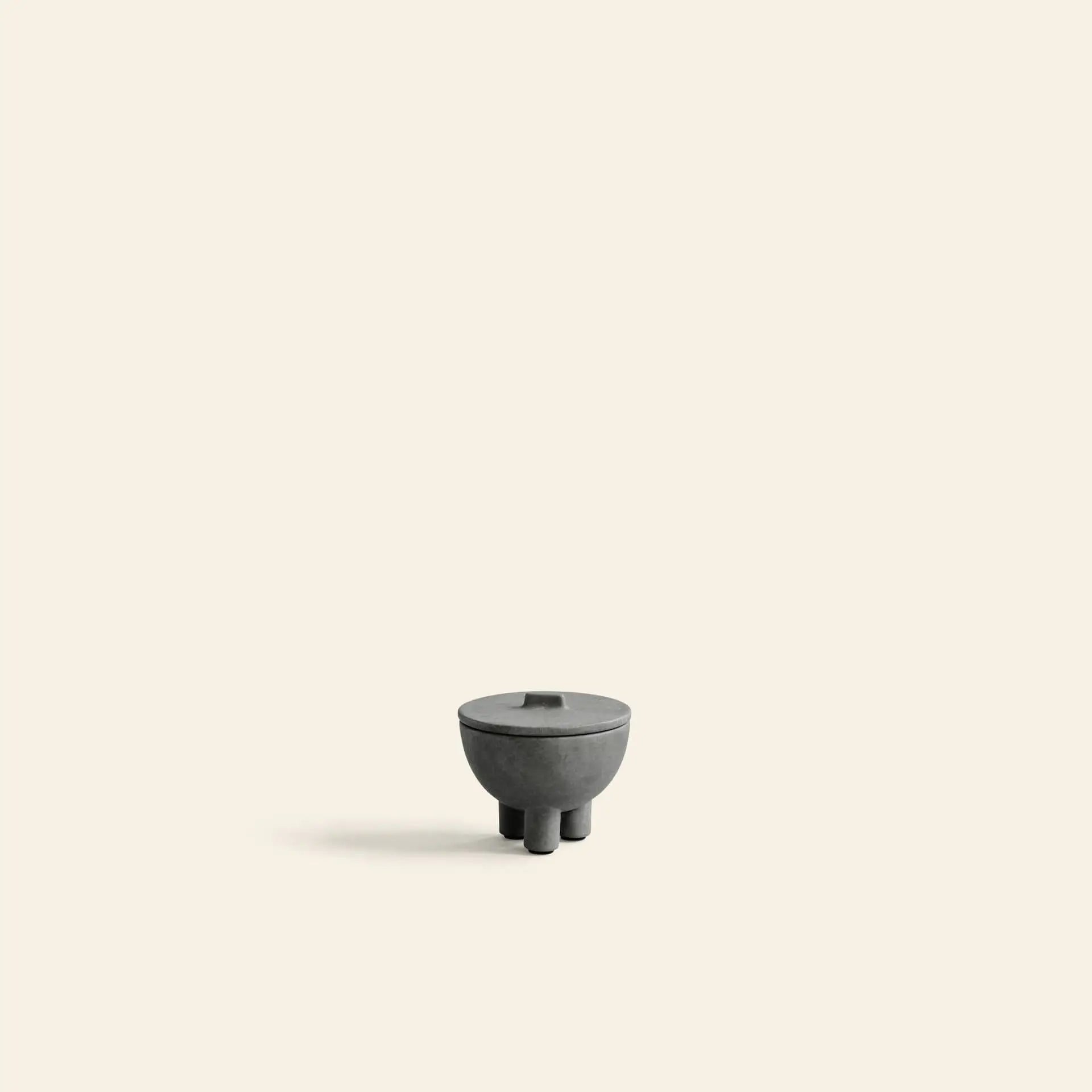 The 101 Copenhagen Duck Jar, Mini—a small, round, dark gray jar with lid and three short legs—sits centered on a light beige background, showcasing the brand’s elegant design as a decorative accent or functional storage piece.