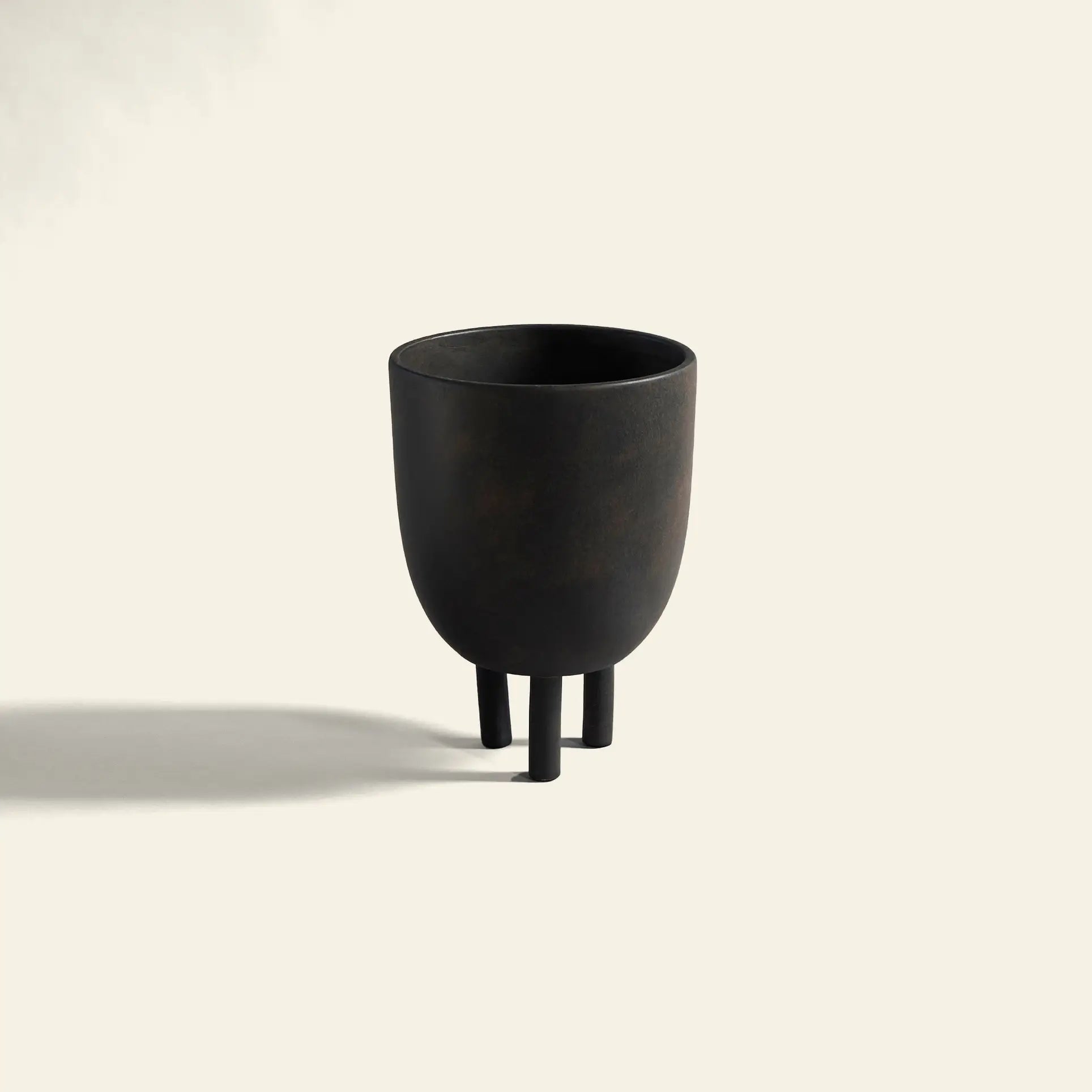 The 101 Copenhagen Duck Pot by 101 Copenhagen is a minimalist black, cup-shaped vessel with three cylindrical legs, casting a shadow on a plain light background and exuding Scandinavian design with subtle whimsical charm.