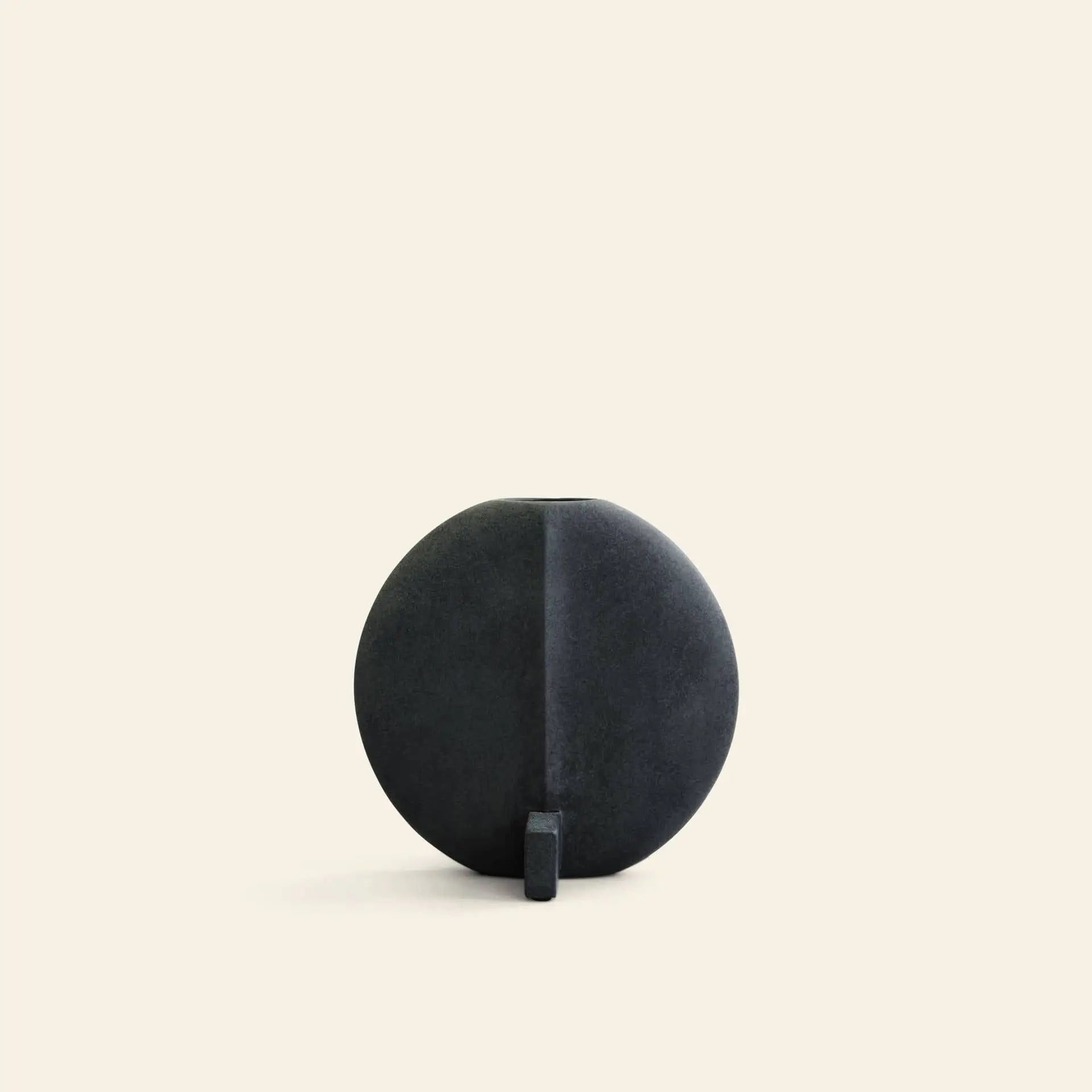 The 101 Copenhagen Guggenheim Vase, Petit by 101 Copenhagen features a round, matte black design with a flat base and small vertical support, set against a light beige background and reflecting subtle art deco influences.