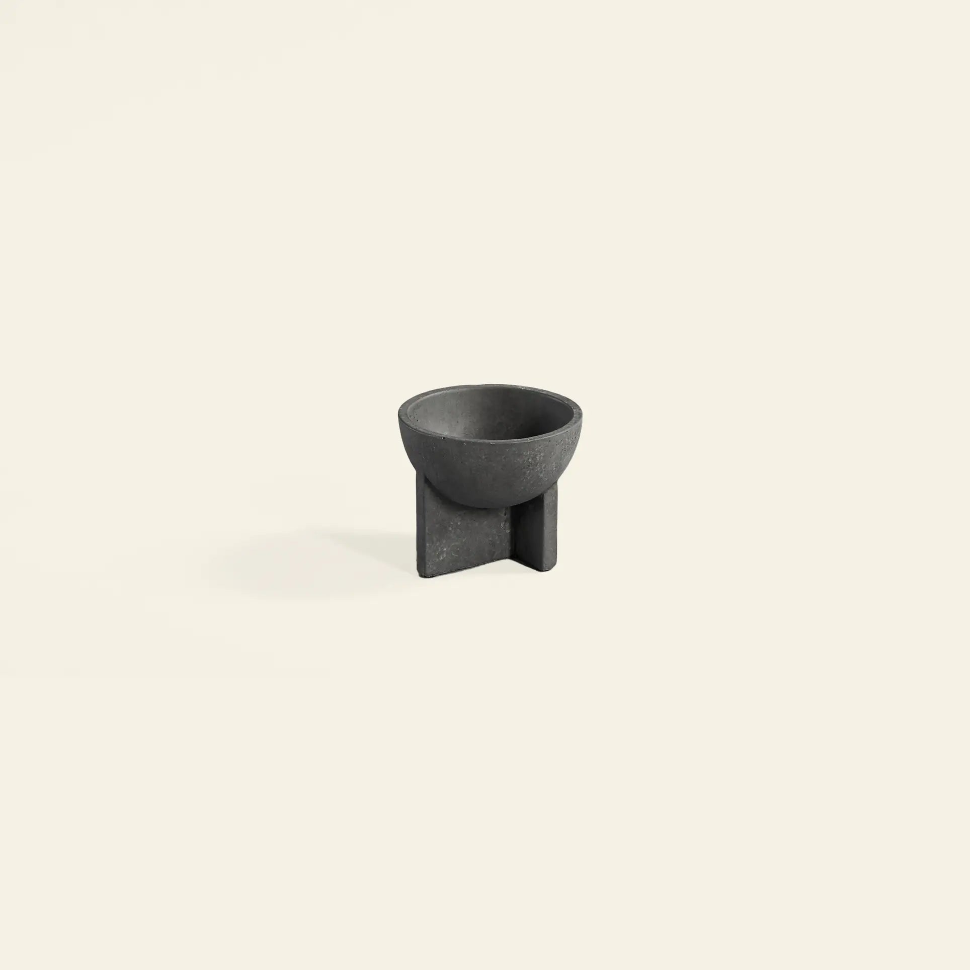 The 101 Copenhagen Osaka Bowl, Mini by 101 Copenhagen is a small modern black fiber concrete bowl with a round top and geometric cross-shaped base, shown against a plain light beige background.