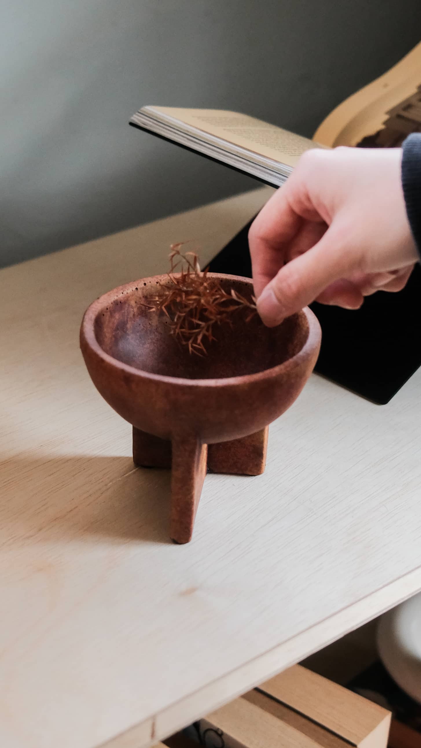 A hand places dried herbs into a 101 Copenhagen Osaka Bowl, Mini by 101 Copenhagen on a light surface, showcasing the sculptural charm of this bowl in everyday rituals.