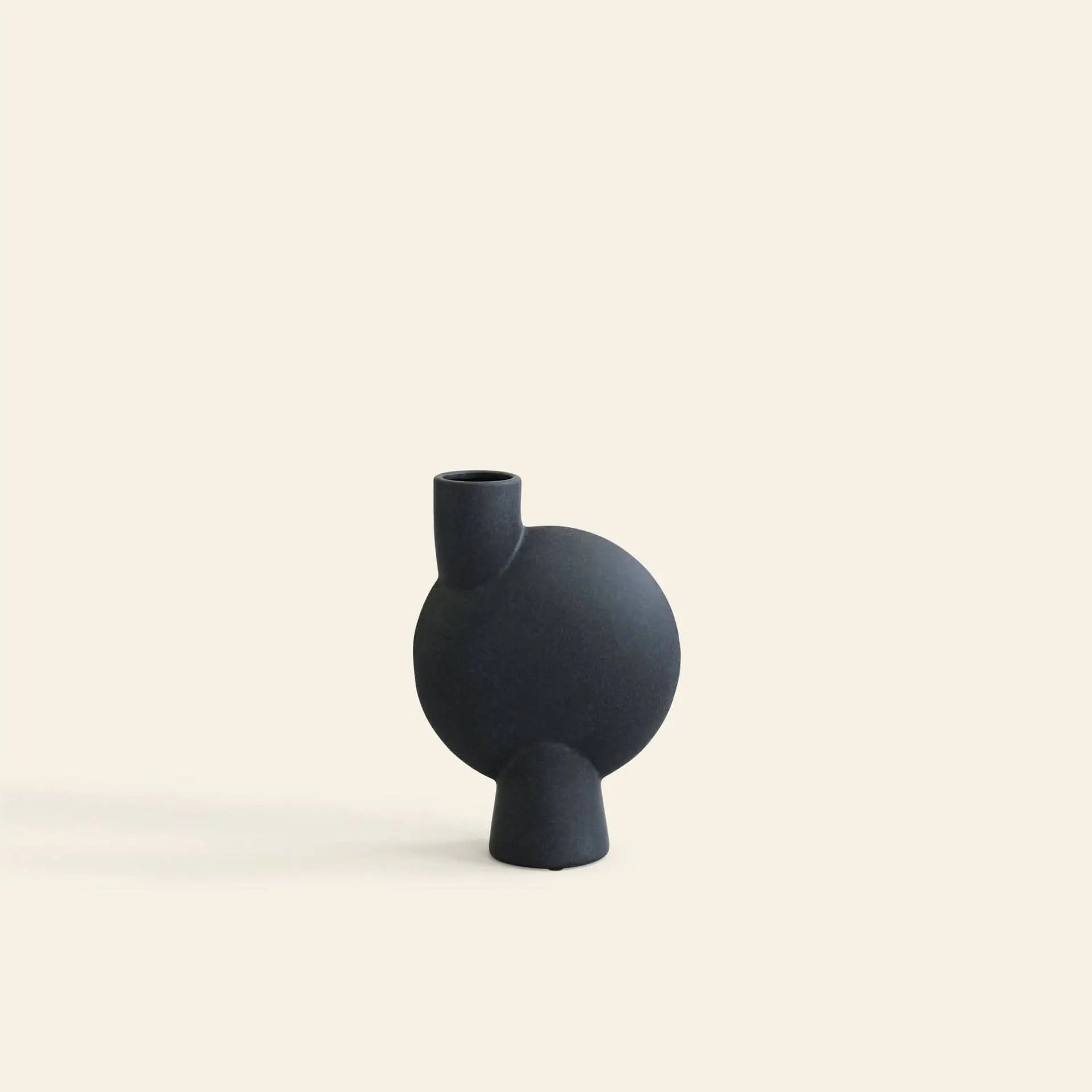 The 101 Copenhagen Sphere Vase Bubl, Medio by 101 Copenhagen is a minimalist matte black ceramic vase with a round body and short angled neck, perfect for adding modern style to your home against a plain off-white background.