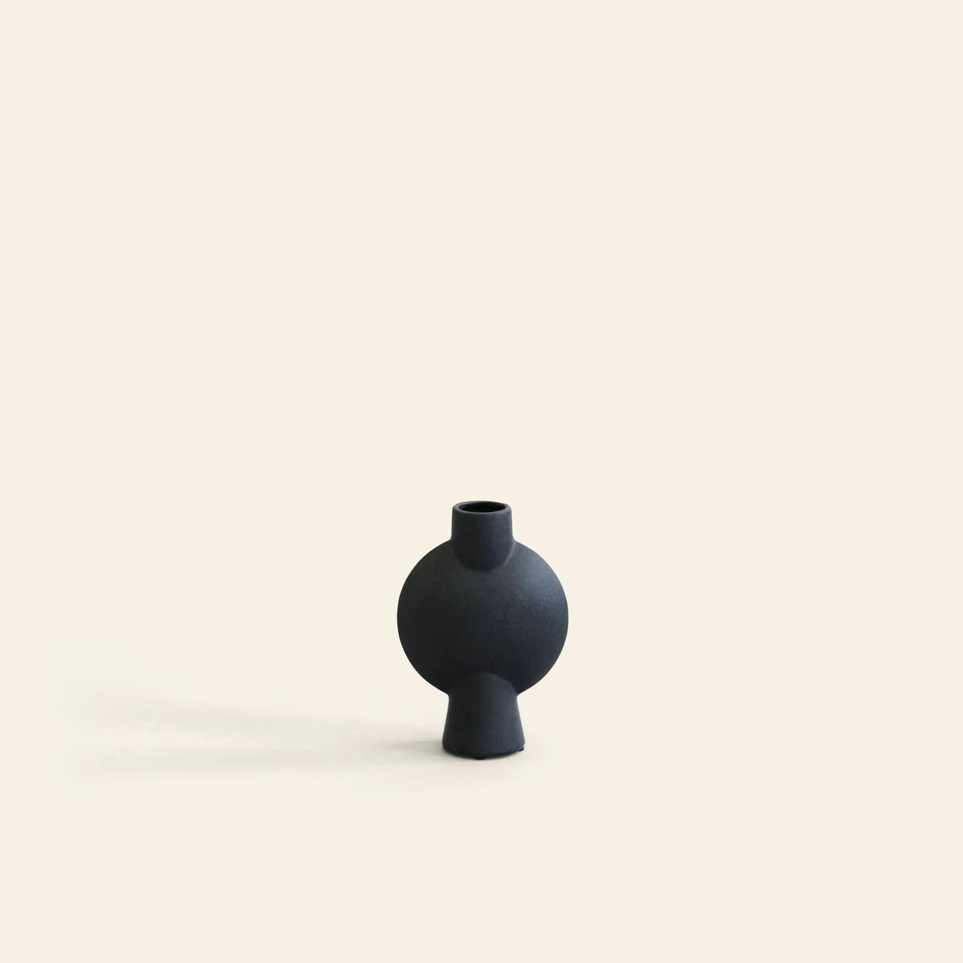 The 101 Copenhagen Sphere Vase Bubl, Mini by 101 Copenhagen features a small, round, matte black geometric design with a narrow neck—an elegant accent for modern décor—displayed on a plain light beige background.