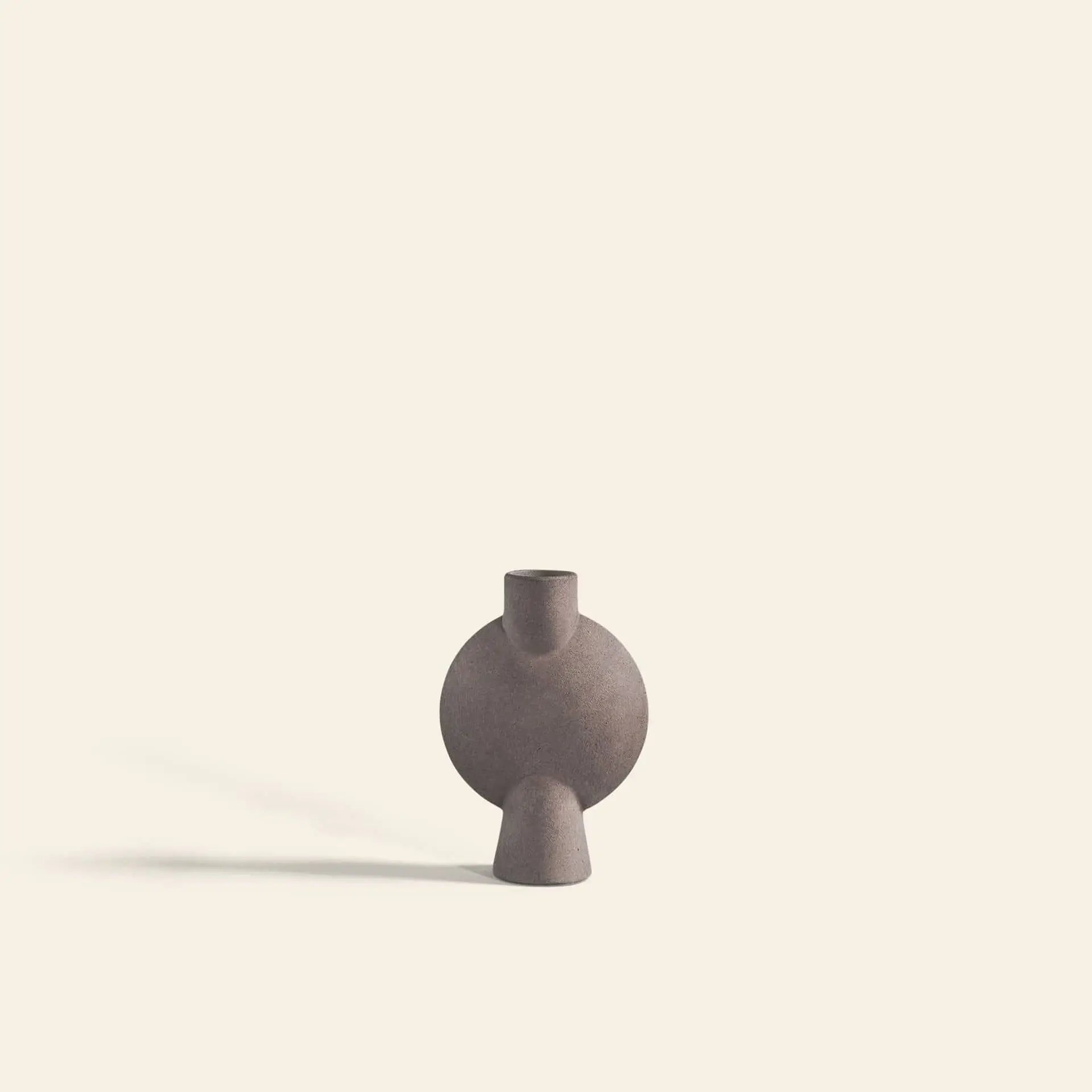 The 101 Copenhagen Sphere Vase Bubl, Mini by 101 Copenhagen is a round, matte brown ceramic vase with a narrow neck and angled base, shown on a light beige background—ideal for modern home décor schemes.