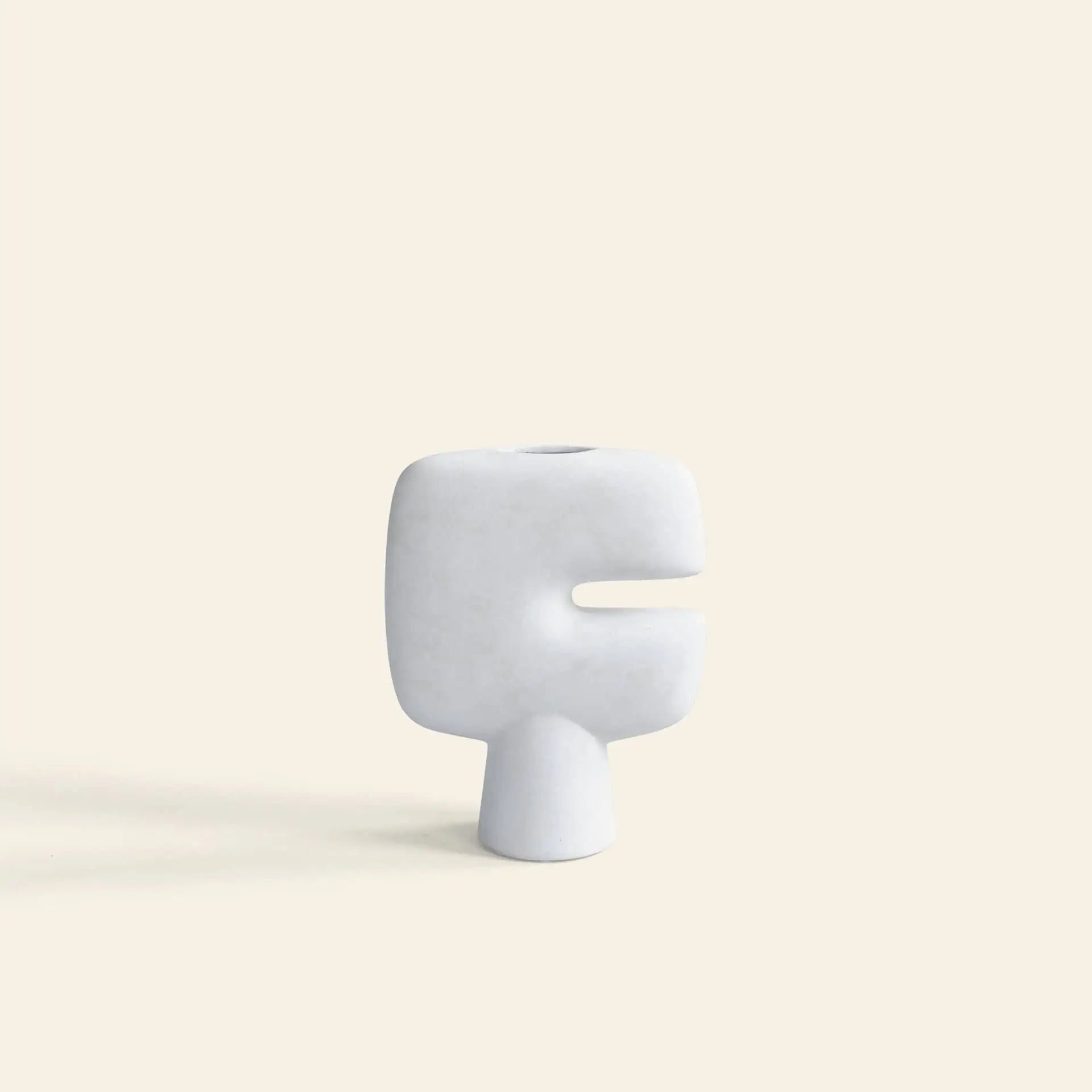 The 101 Copenhagen Tribal Vase, Mini by 101 Copenhagen features a minimalist white ceramic finish, a geometric abstract shape, and a horizontal cutout, displayed against a plain beige background.