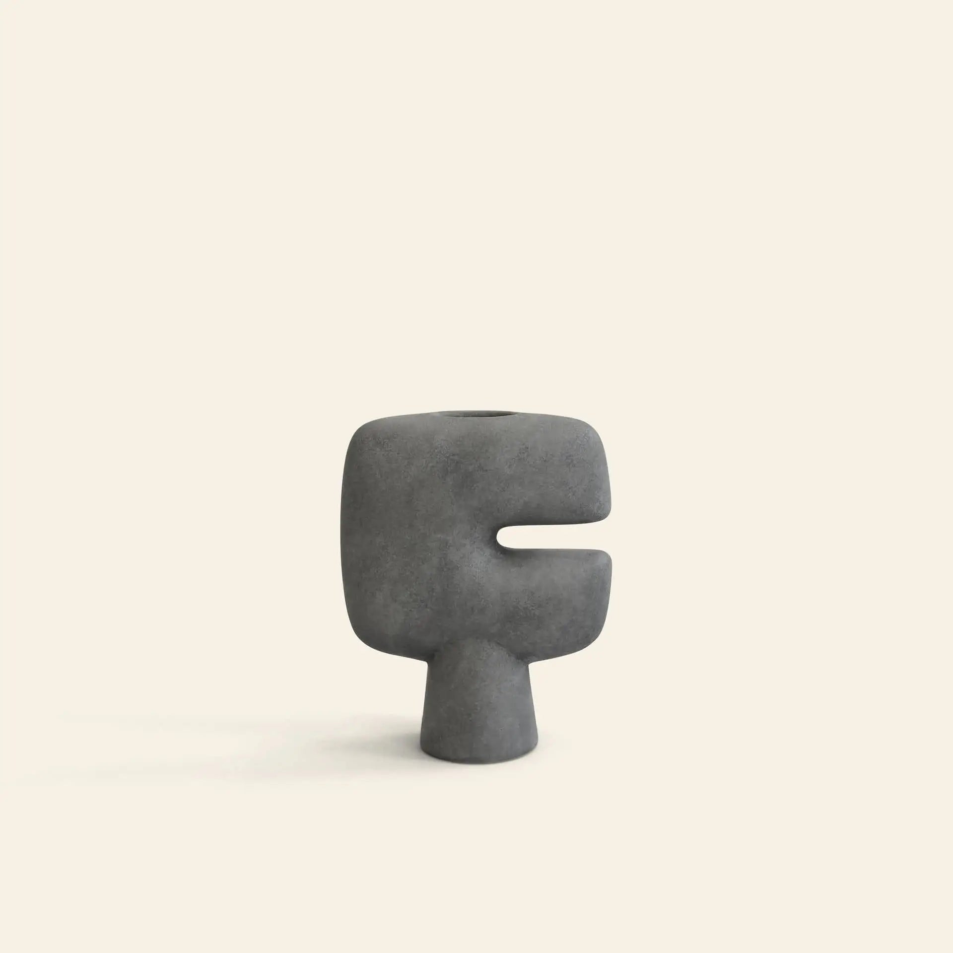 The 101 Copenhagen Tribal Vase, Mini by 101 Copenhagen is a minimalist, abstract gray ceramic vase with a geometric shape, wide body, and horizontal cutout, displayed against a plain beige background.