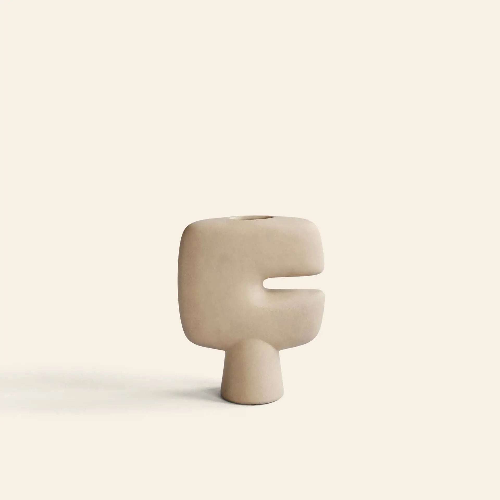The 101 Copenhagen Tribal Vase, Mini by 101 Copenhagen is a minimalist beige vase with a tribal-inspired abstract shape, rounded edges, and a slit-like opening, shown against an off-white background.