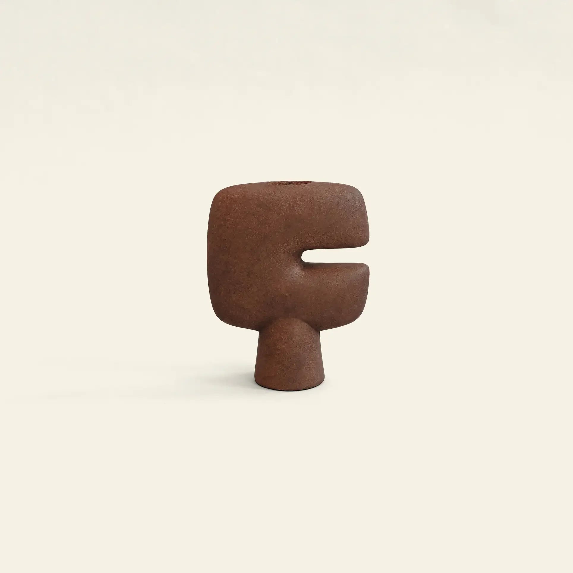 The 101 Copenhagen Tribal Vase, Mini by 101 Copenhagen is a small, abstract brown ceramic piece with a rounded top, central notch cutout, and narrow base, resembling a minimalist face against a plain light background.