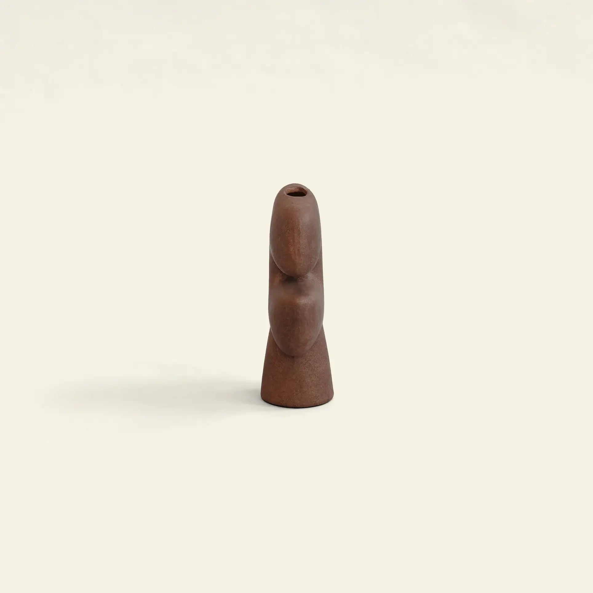 The 101 Copenhagen Tribal Vase, Mini by 101 Copenhagen is a small, abstract wooden sculpture with smooth curves and an opening at the top, standing upright against a plain, light background.