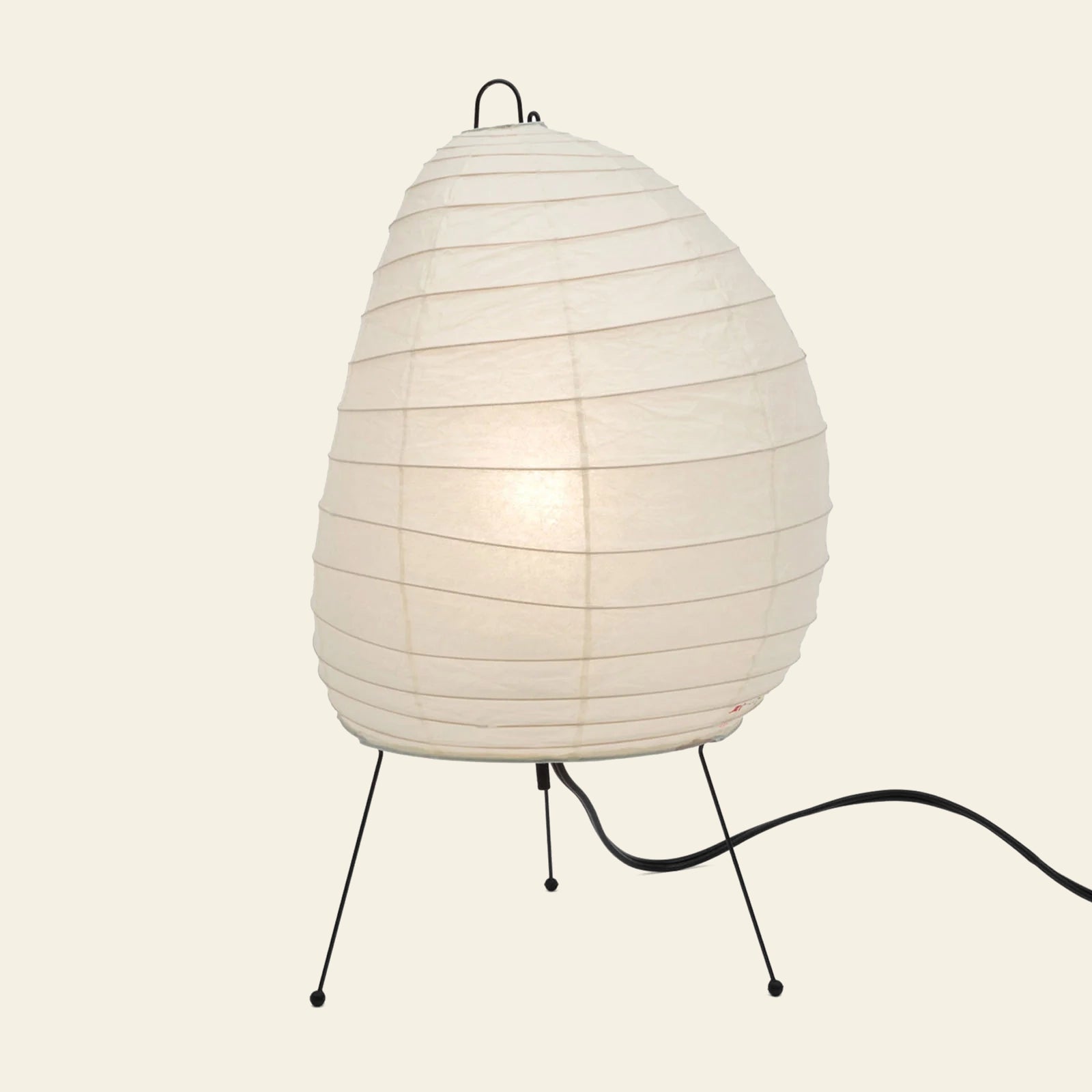 The Akari 1N by Akari is a white, oval paper lantern lamp with slim metal legs and a black power cord, glowing gently against a plain background—a modern design inspired by Akari Light Sculptures.