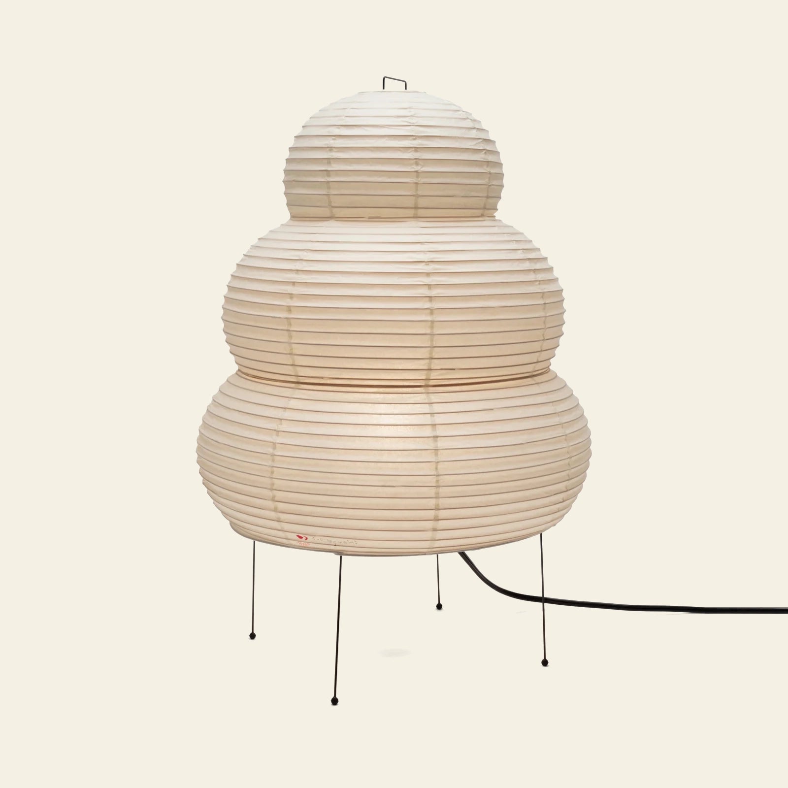 The Akari 24N by Akari features three stacked, ribbed washi paper tiers atop slim black metal legs, with a black cord extending from the base, shown against a plain light background and reflecting Japanese craftsmanship.