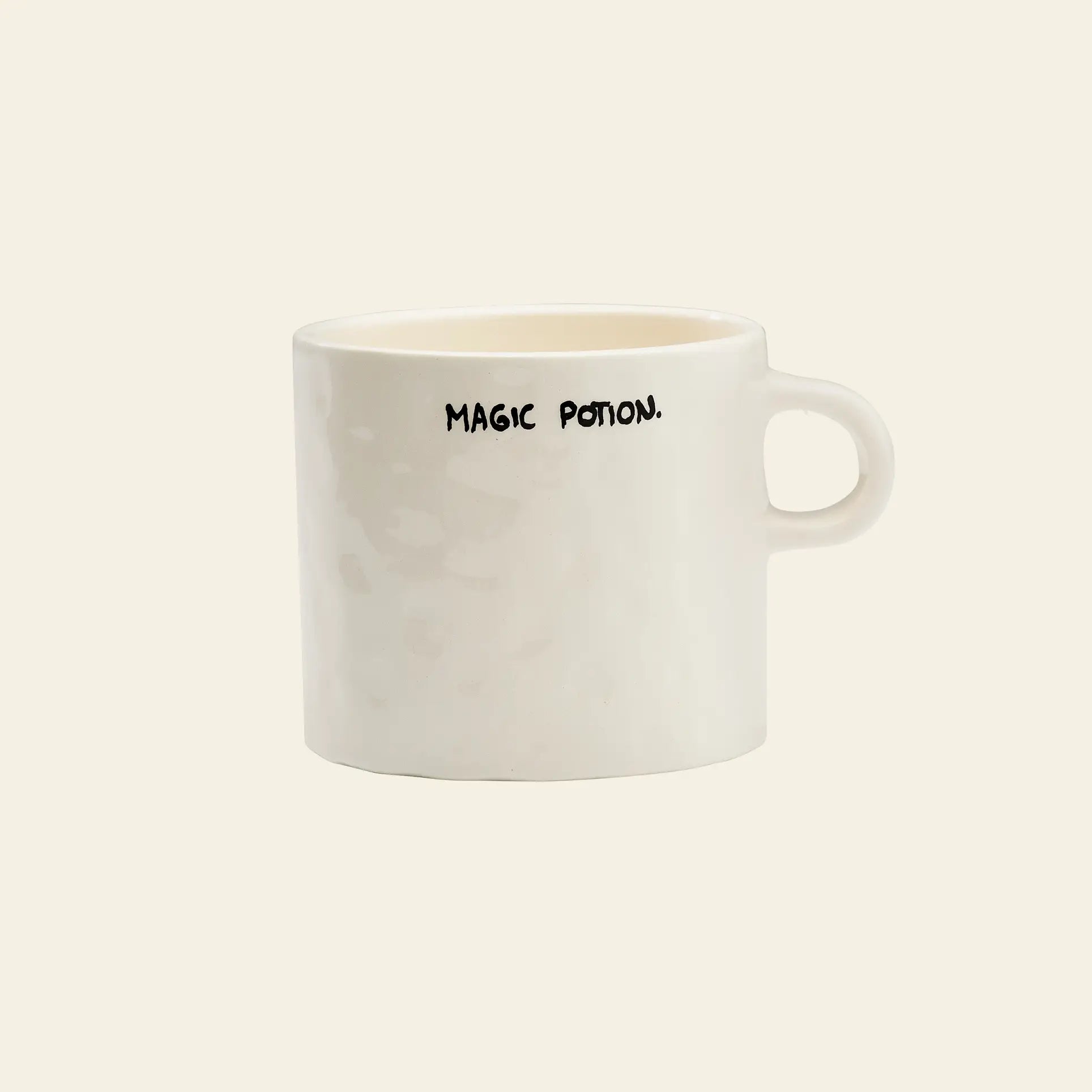 The Anna + Nina Magic Potion Mug is a plain white mug by Anna + Nina, featuring MAGIC POTION. in black uppercase letters near the rim, and is perfect for your next brew against a simple, light background.