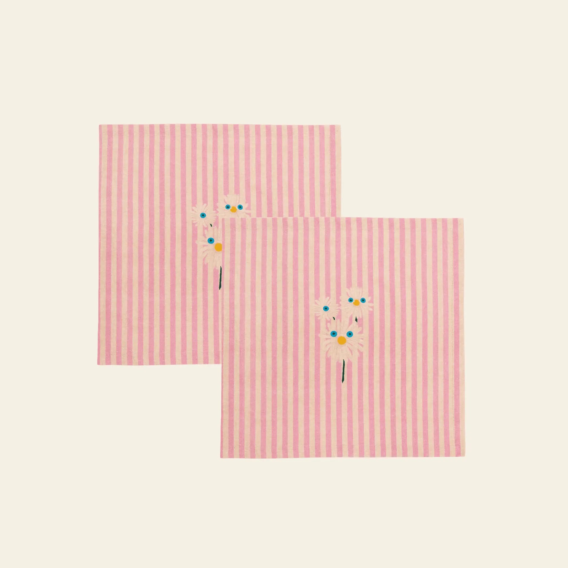 The Anna + Nina Trippy Flower Napkin set includes two pink and white striped cloth napkins, each adorned with embroidered daisies, bringing a cheerful floral touch to your spring table.