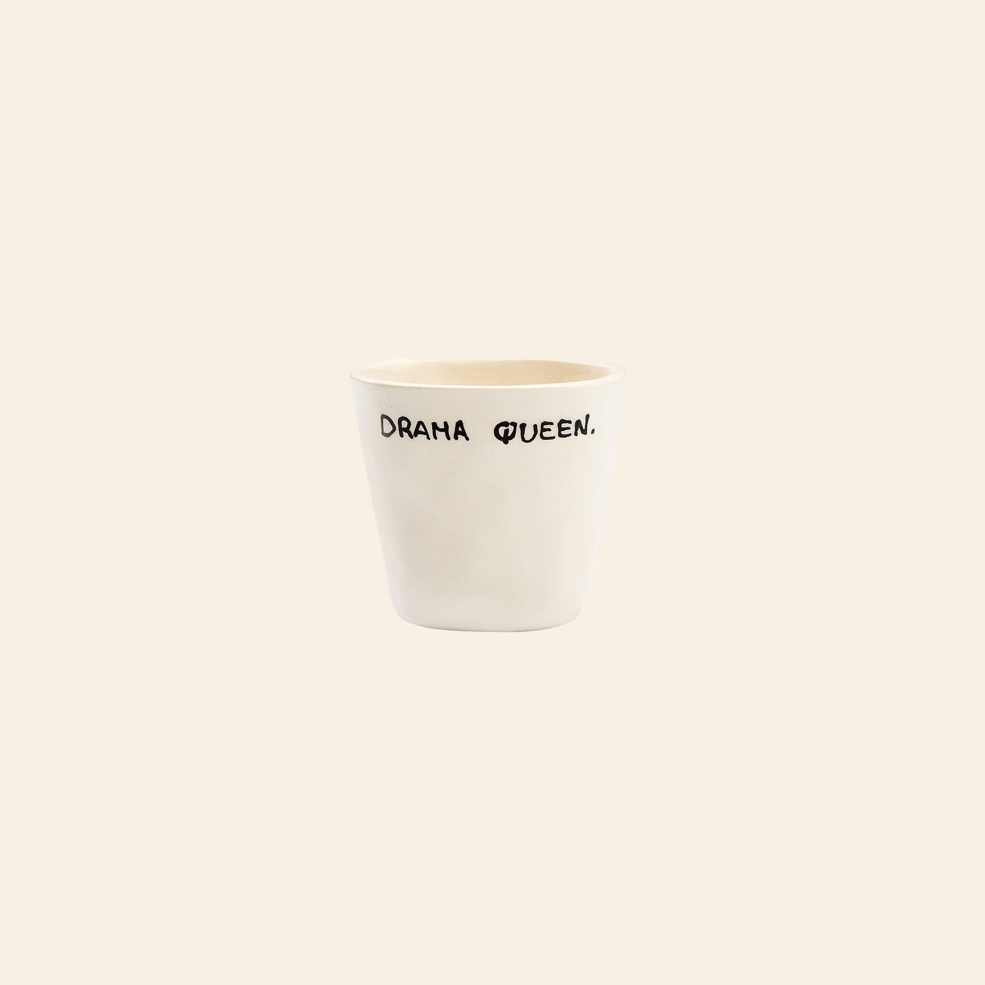 The Anna + Nina Drama Queen Espresso Cup is a white ceramic cup with DRAMA QUEEN. in playful black lettering on a light beige background—a bold, stylish touch for your coffee moments.
