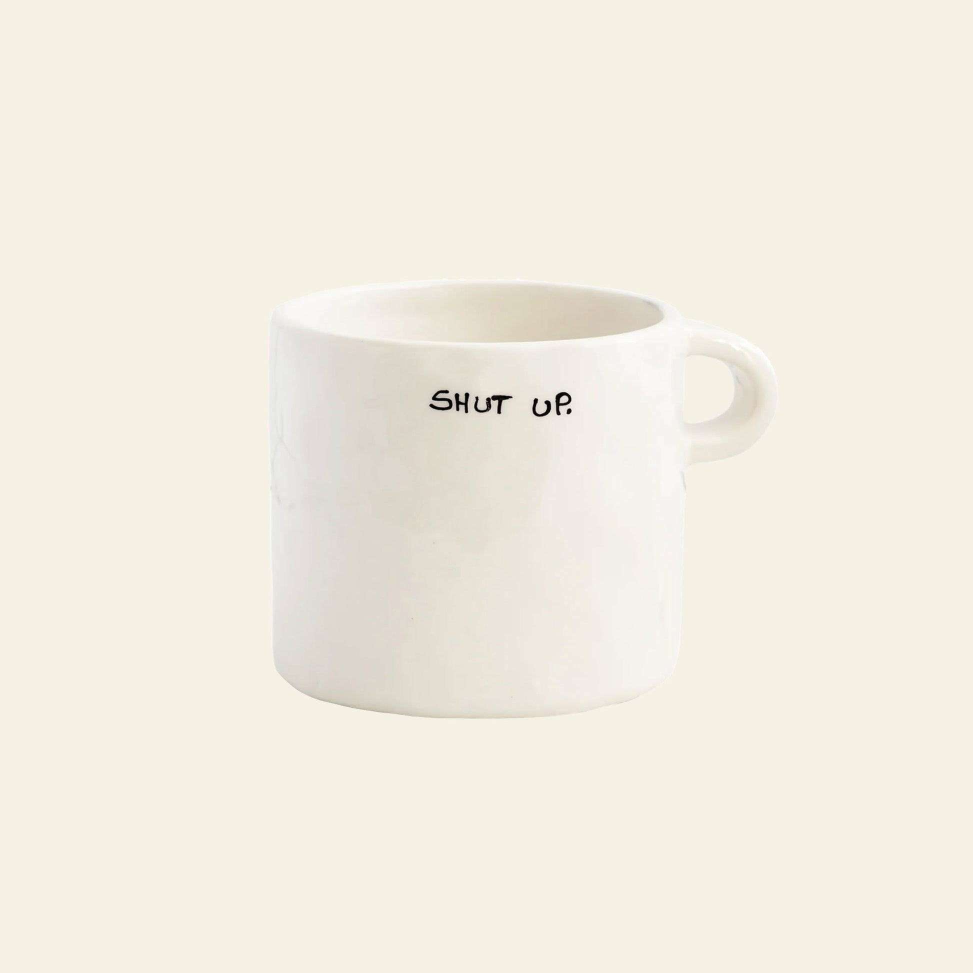 The Anna + Nina Shut Up Mug is a white ceramic mug with a small handle and bold black SHUT UP. text on the side—ideal for your daily caffeine fix.