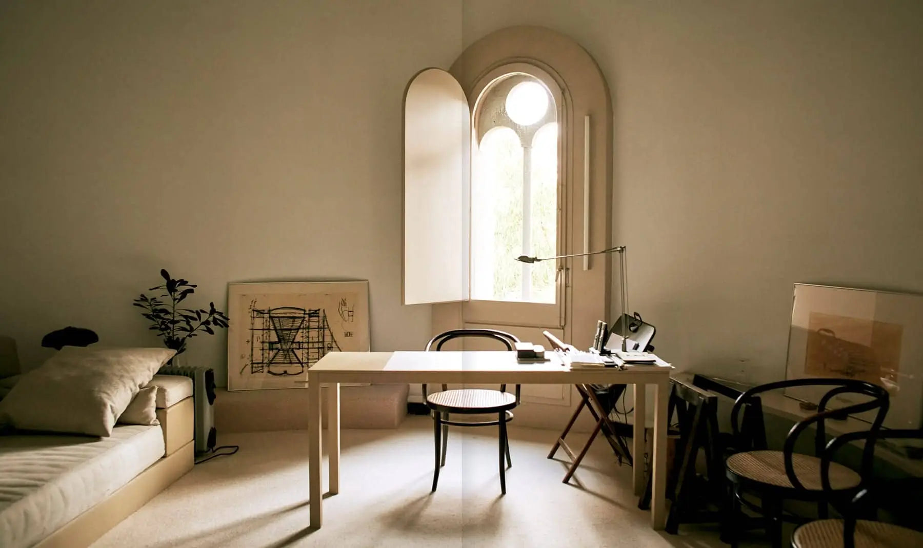 A bright room with a tall arched window, modern desk, and scattered office supplies channels the cozy, minimalist spirit of industrial reuse found in Apartamento La Fábrica, Ricardo Bofill by Apartamento.