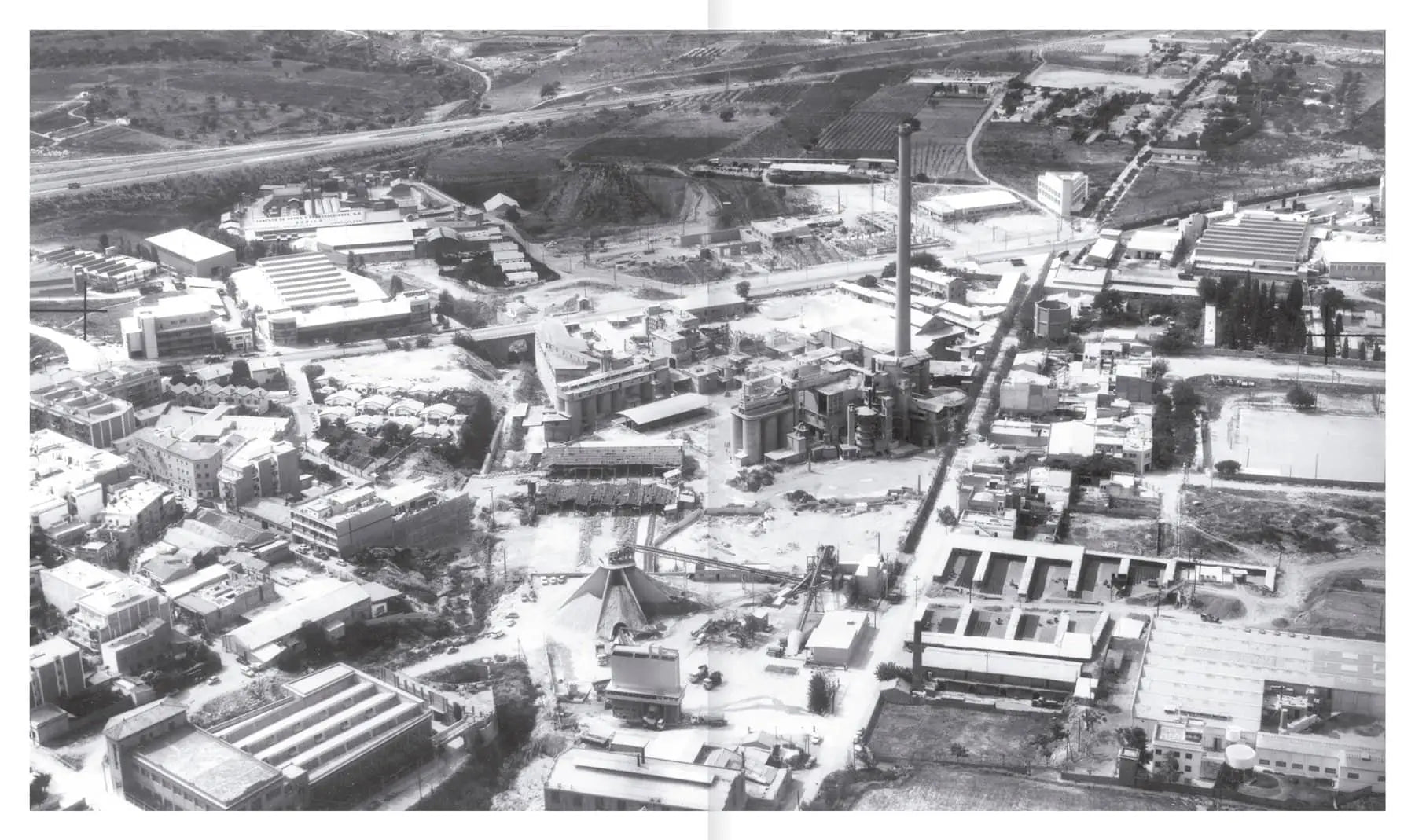 A black-and-white aerial view of an industrial complex—factories, warehouses, chimneys, and tracks—reflecting the adaptive reuse found in Apartamento La Fábrica by Ricardo Bofill, from Apartamento.