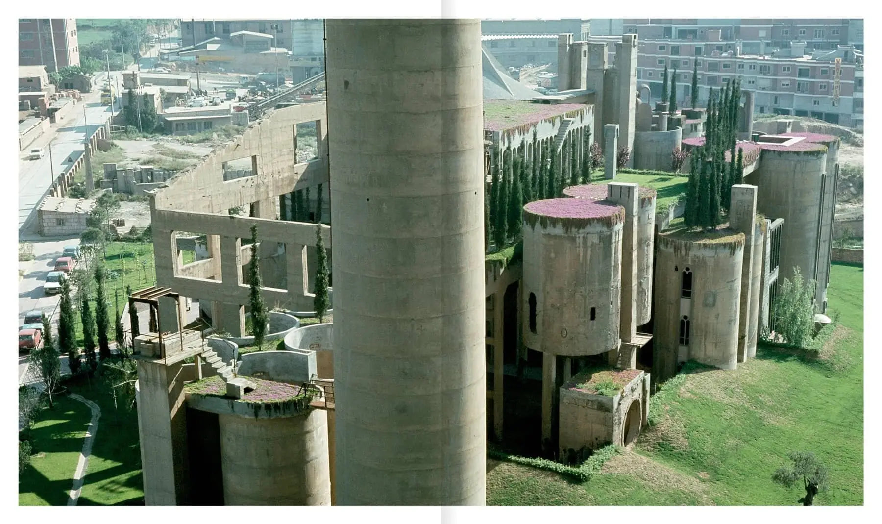Apartamento’s La Fábrica by Ricardo Bofill features a large abandoned cement factory with cylindrical towers and overgrown vegetation, showcasing striking industrial reuse within the urban landscape.