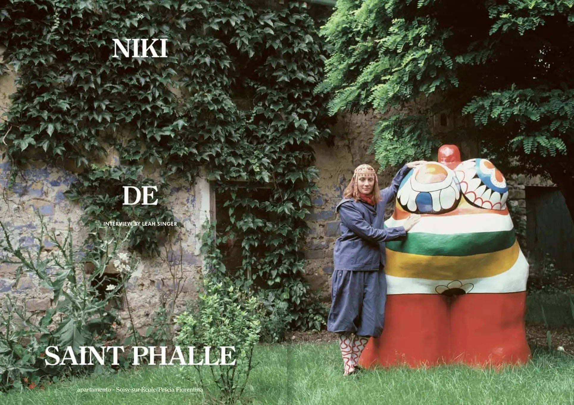 A woman in a blue dress and patterned boots embraces an abstract sculpture in a lush garden, with a stone wall behind her. Large white text reads Apartamento, echoing the style of Apartamento Magazine Issue #28s cover.