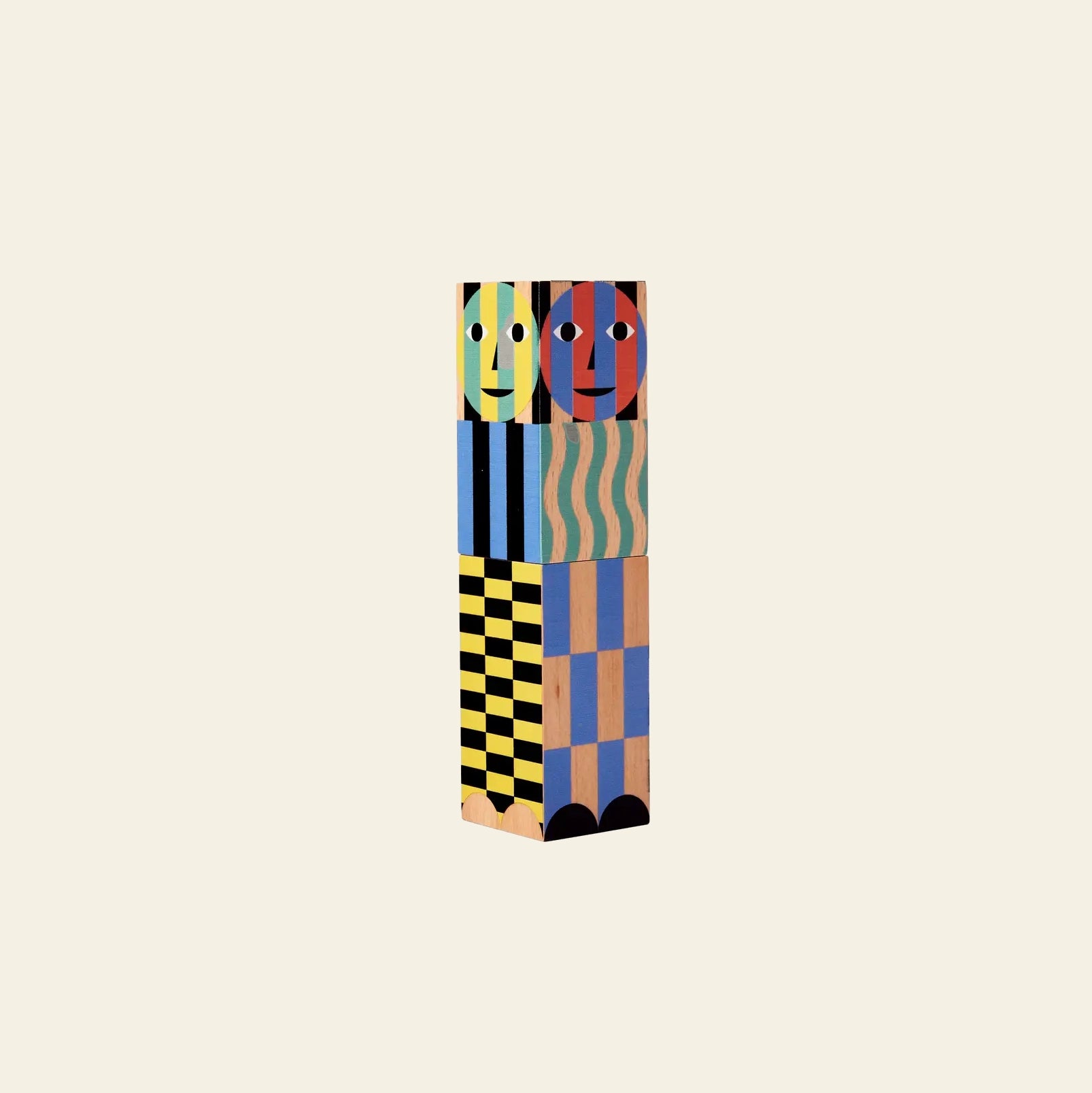 The Areaware Everybody Grinder by Areaware is a tall, rectangular wooden grinder painted with bold geometric patterns and vivid colors, featuring two stylized faces at the top—perfect for adding creative flair to any plain cream background.