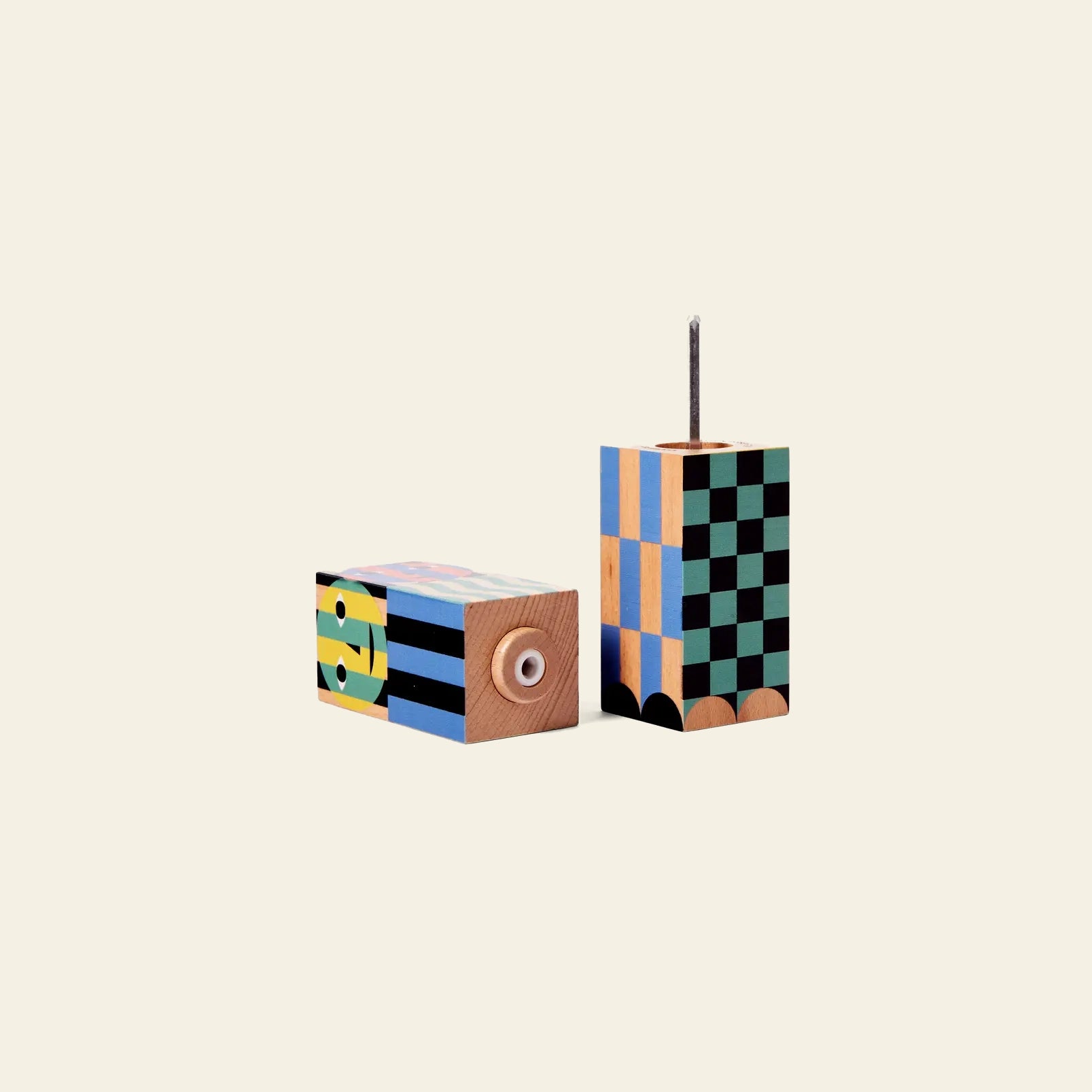 The Areaware Everybody Grinder by Areaware features two vibrant, geometric-patterned wooden grinders—one with a circular eye motif, the other upright with a metal rod—adding playful color and style to any light-toned setting.