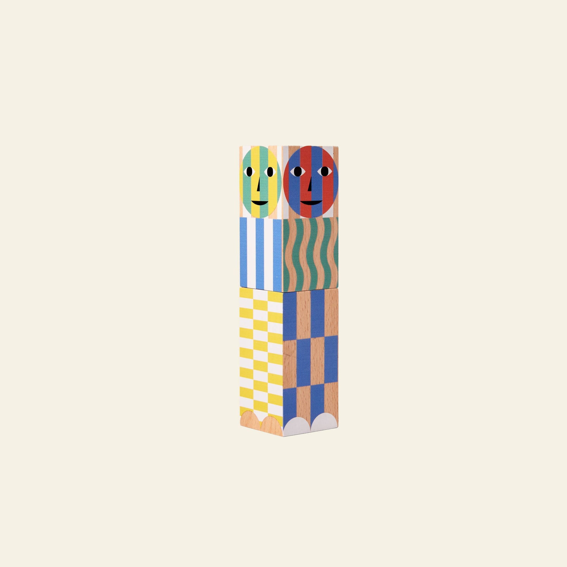 The Areaware Everybody Grinder by Areaware is a playful kitchen tool featuring two faces on the top block and geometric patterns in yellow, blue, green, and white on a plain light background.