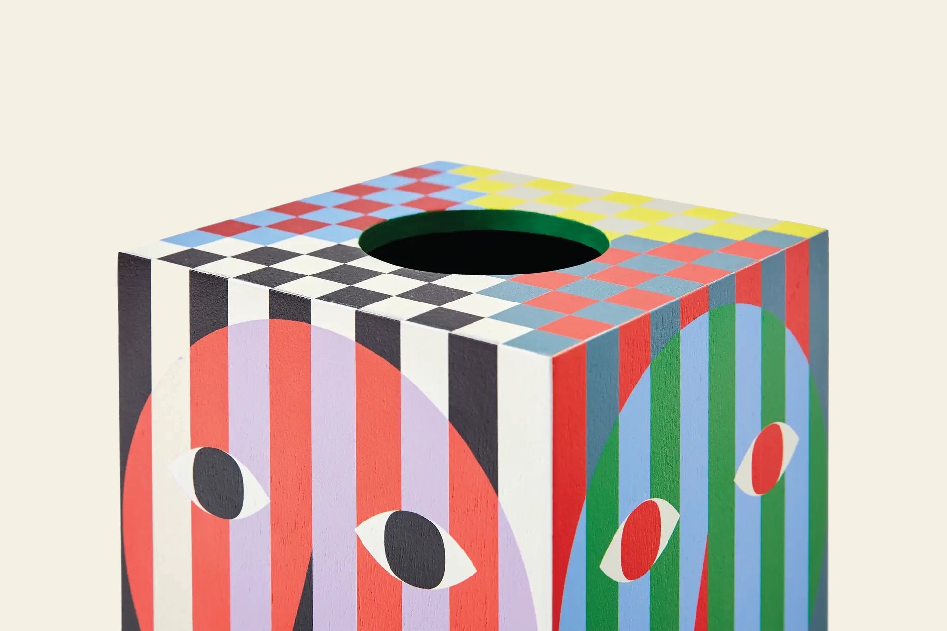 The Areaware Everybody Tissue Box features a bold, colorful geometric design with stripes, checkerboard patterns on top, and abstract eye shapes in red, purple, green, and blue on a light cream background.