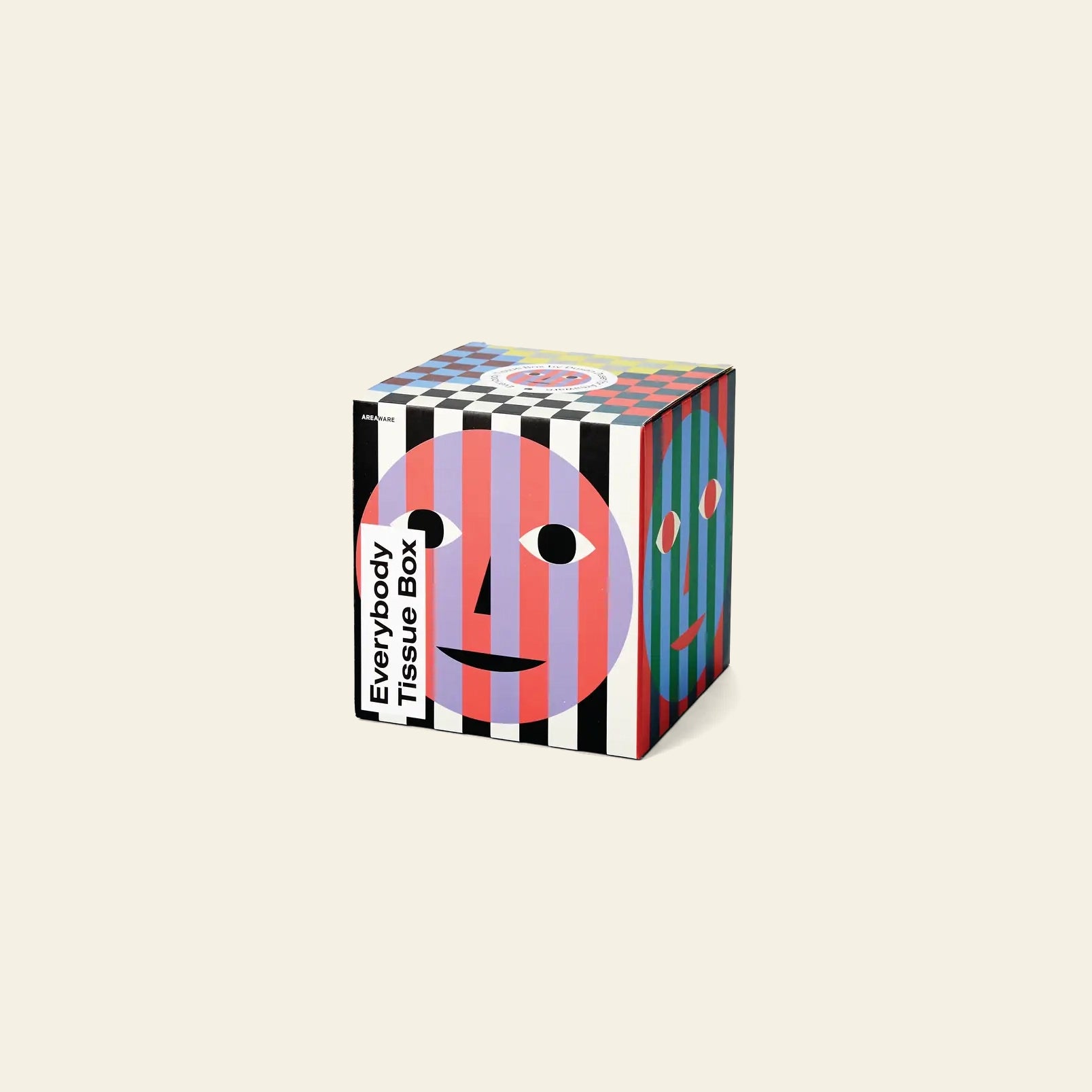 The Areaware Everybody Tissue Box features bold, colorful stripes and abstract pink, blue, and red faces on a square cover. Everybody Tissue Box is printed on one corner against a plain beige background.
