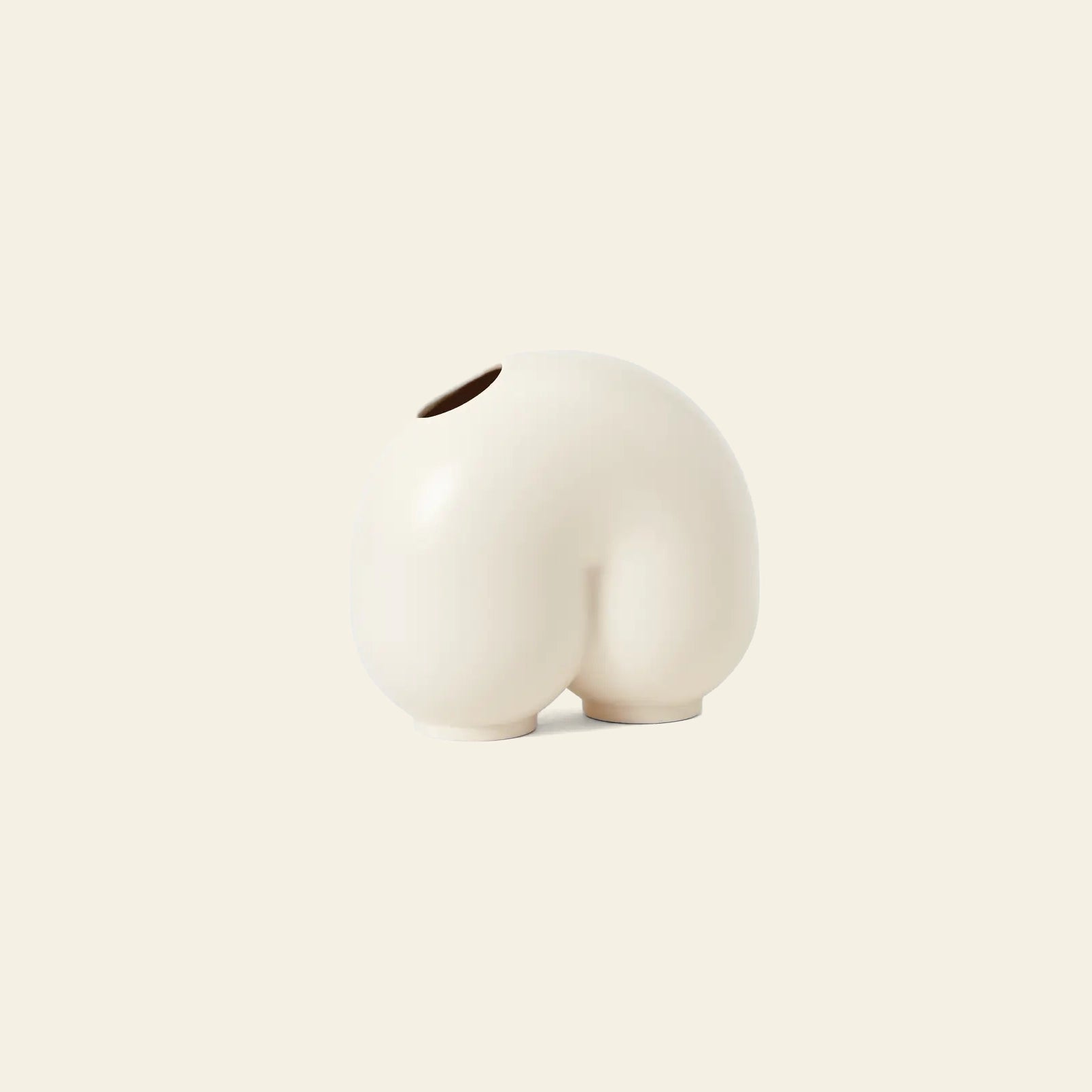The Areaware Kirby Vase Enny by Areaware is a round, off-white ceramic vase shaped like a pair of buttocks with a top opening—perfect as a quirky bud vase for unique floral arrangements, shown against a plain beige background.