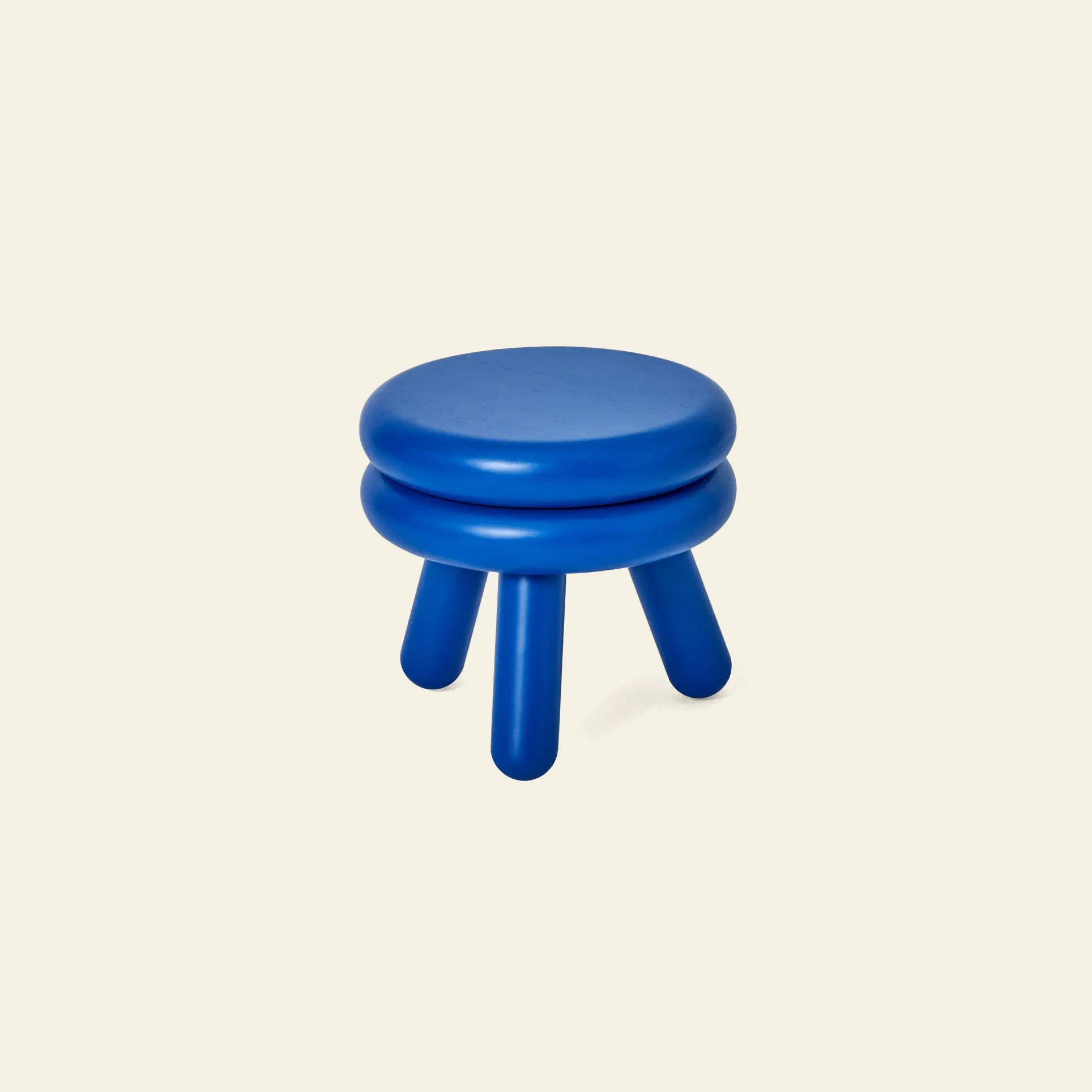 The Areaware Pluma Stool Short by Areaware is a small, round, blue stool with a contemporary design, three thick cylindrical legs, and a double-layered seat set against a plain light beige background.