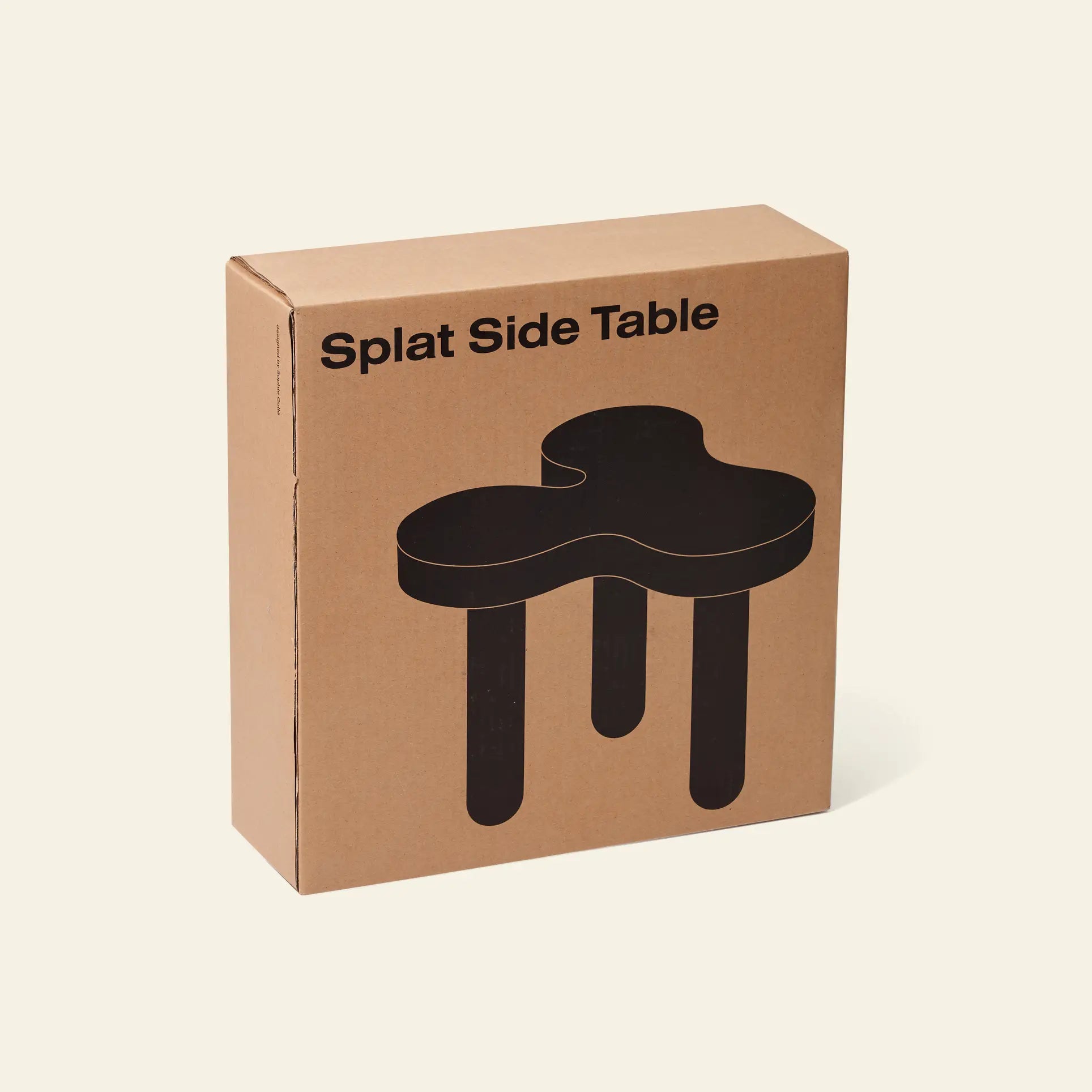 A brown cardboard box displays Areaware Splat Side Table Short and a bold black illustration of this Areaware table, featuring an irregular splat-shaped top with three chunky legs in a unique layout, set against a plain light background.