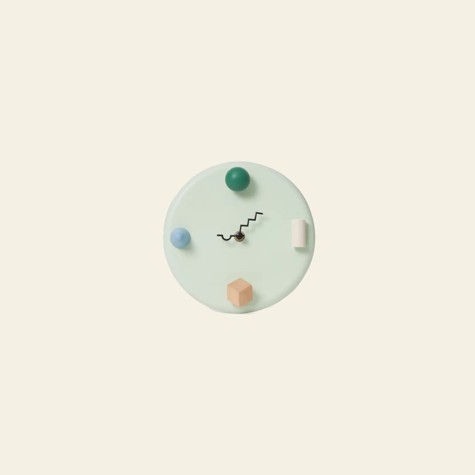The Areaware Wall Clock by Areaware features a minimalist pale circular face with abstract 3D geometric markers in blue, green, peach, and white, plus black zigzag hands, all set against a plain beige background.