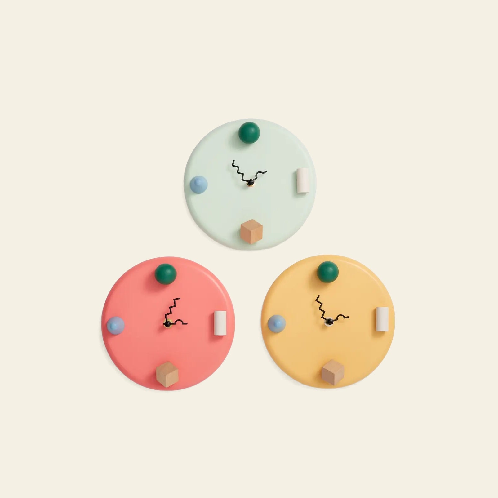 Areaware Wall Clock by Areaware features abstract geometric hour markers and zigzag black hands. In mint green, coral pink, and yellow, these clocks add a whimsical touch to any space against a light beige background.