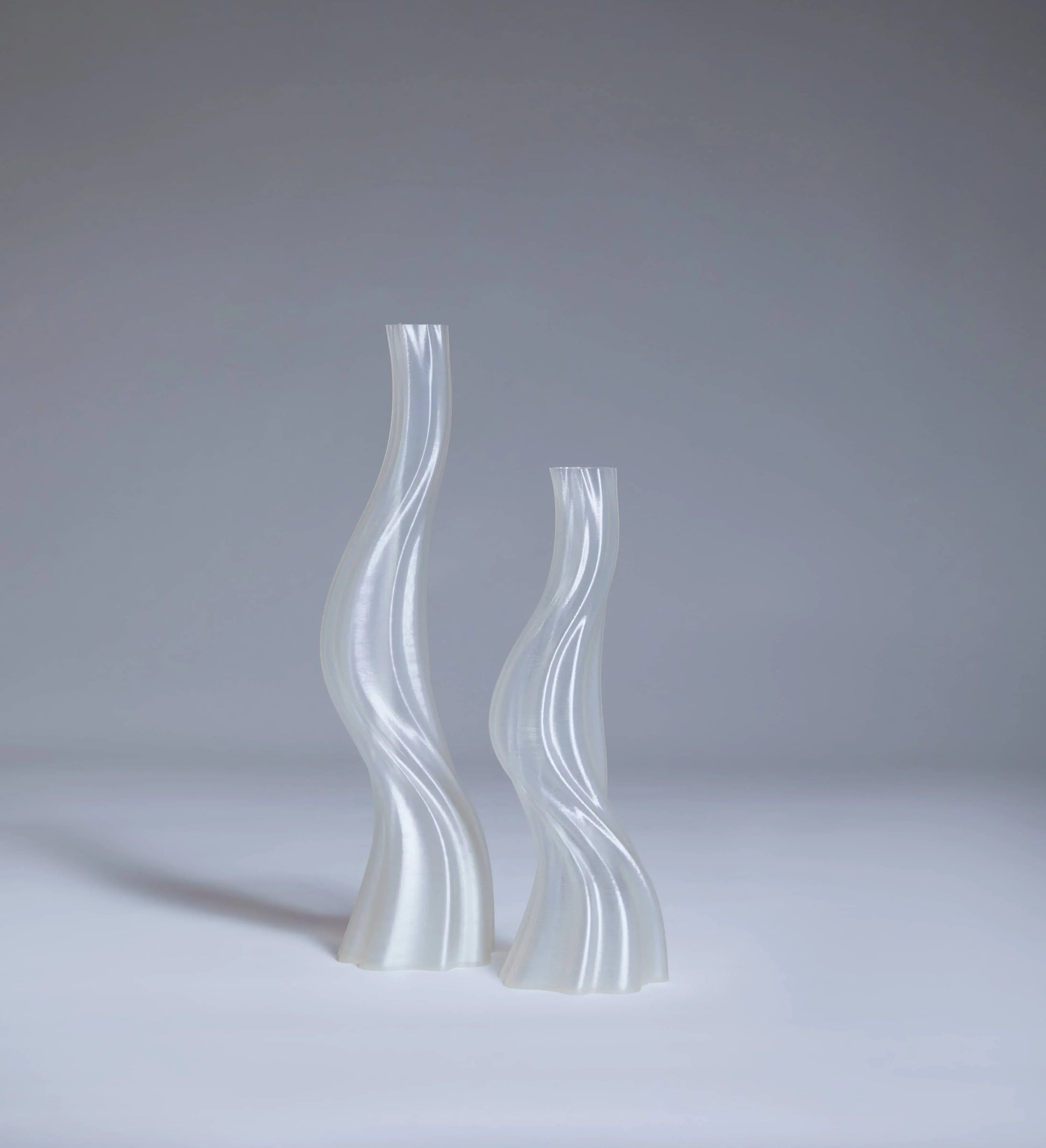 Two translucent Argot Studio Les Hortenses Vases, Small, with elegant curves and modern abstract design, stand side by side on a light surface against a pale gray background—a contemporary 3D-printed reinterpretation.
