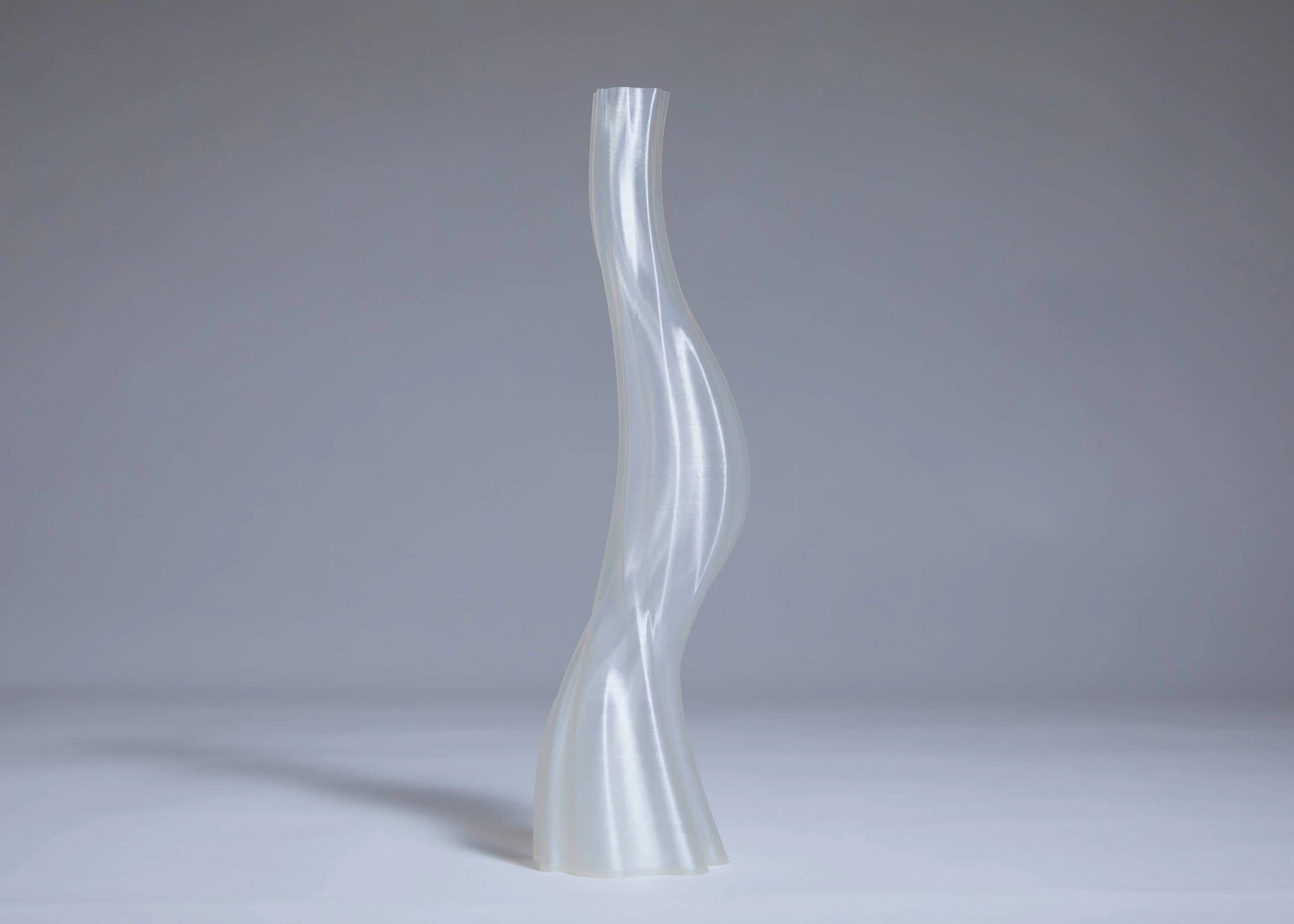 The Argot Studio Les Hortenses Vase, Tall stands upright on a plain light surface with a gray background, showcasing its translucent and wavy 3D-printed form.
