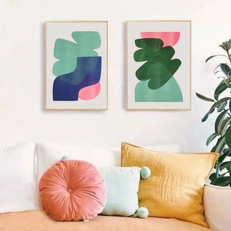 Two Bbblob Sundown & Horizon (2020) Riso prints (30x42) in green, blue, and pink hang above a white couch with colorful pillows. A leafy plant to the right completes this sunset-inspired decor from Bbblob.