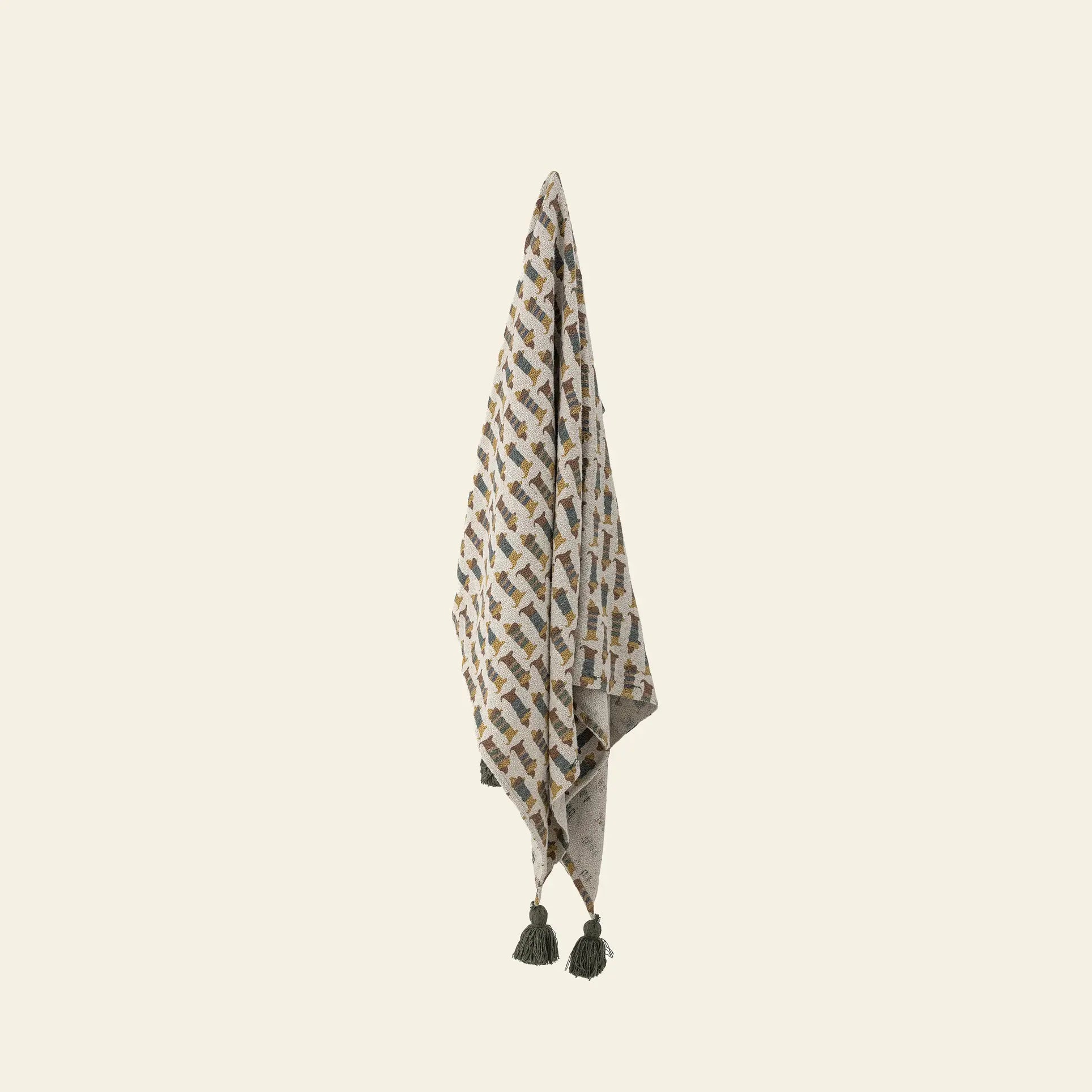 The Bloomingville Charlie Throw by Bloomingville is a recycled cotton throw with a geometric earth-tone pattern and two dark green tassels at each bottom corner, displayed vertically against a light background.