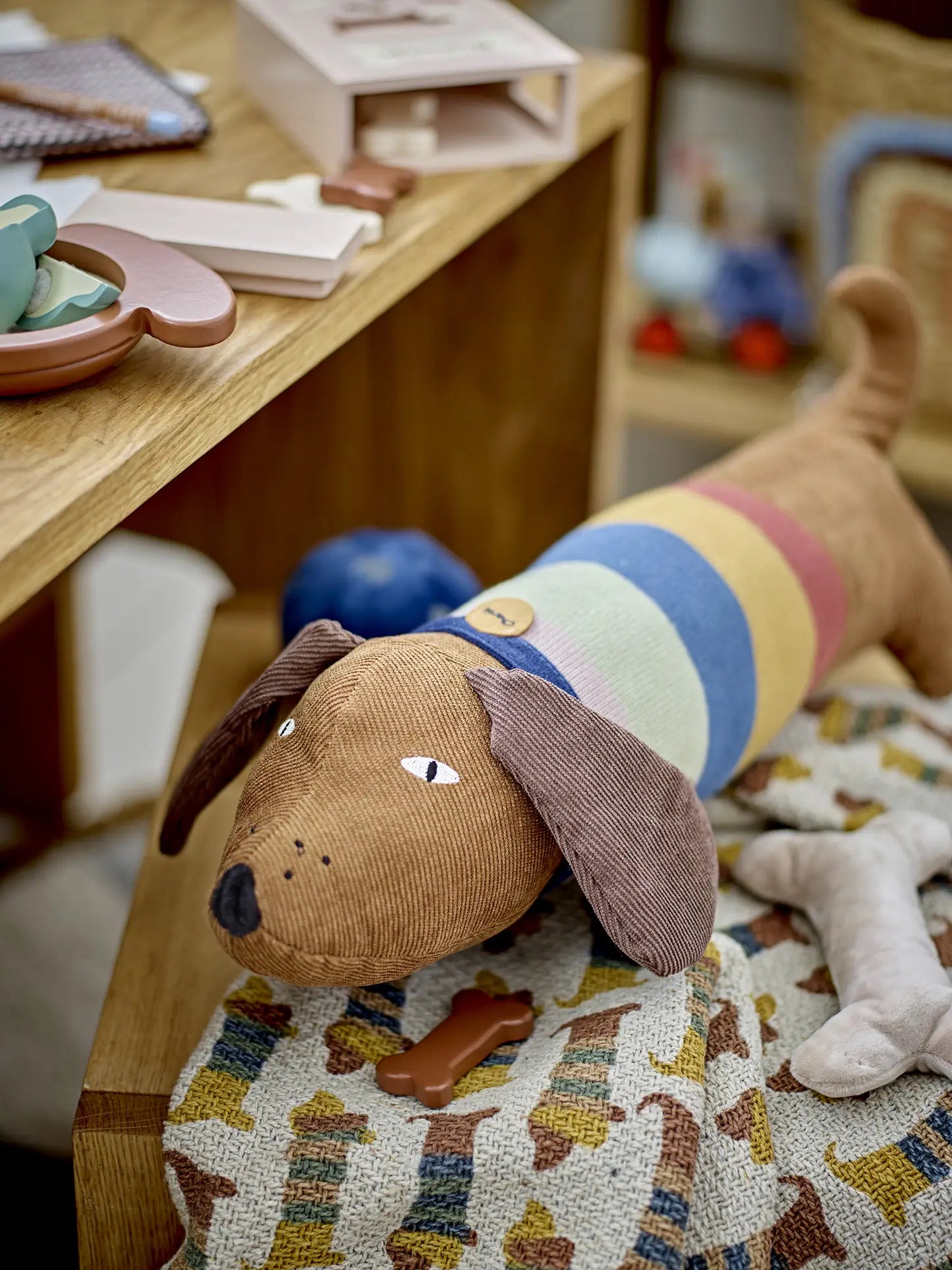 A plush dog toy with a brown head and floppy ears rests on the Bloomingville Charlie Throw, near a wooden table with small Bloomingville MINI toys and objects.