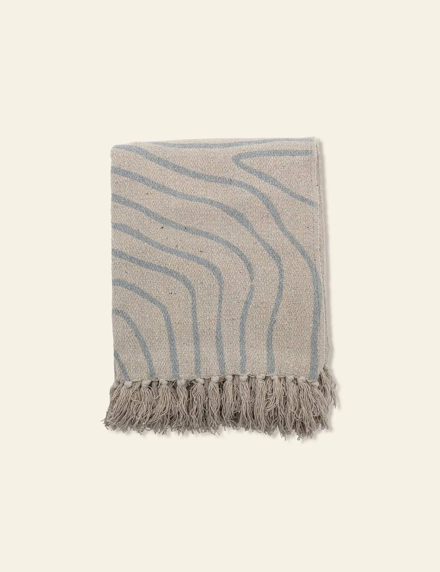 The Bloomingville Dami Throw by Bloomingville is a folded soft blanket made from recycled cotton, featuring subtle wavy blue lines and fringed tassels on one edge, displayed on a light background for sustainable style.