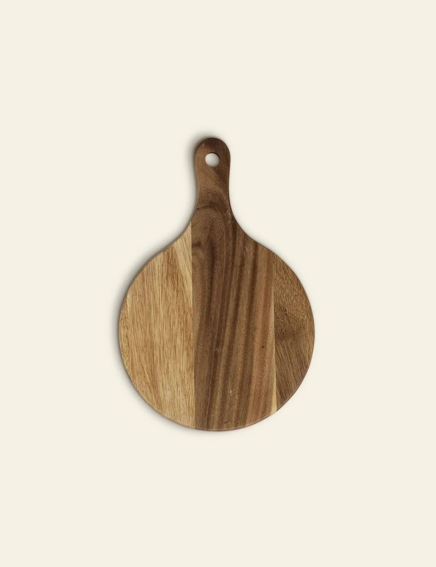 The Bloomingville Dana Cutting Board by Bloomingville is a round beech wood board with a handle and small hole, featuring striped wood tones—an elegant addition to any kitchen, shown on a plain light background.