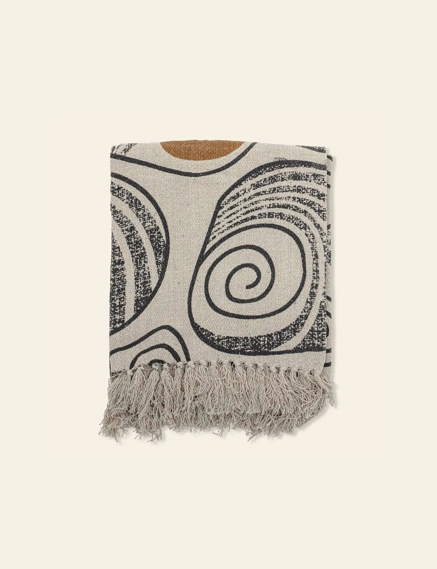 The Bloomingville Giano Throw by Bloomingville is a beige blanket made from recycled cotton with black and brown abstract swirl patterns and a fringe trim, adding cozy style to any room.