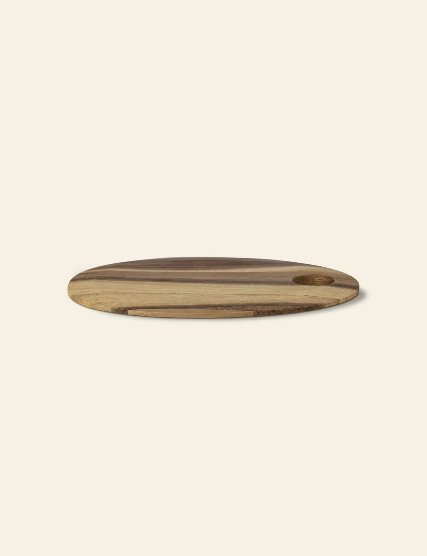 The Bloomingville Guti Cutting Board by Bloomingville is a round suar wood kitchen accessory with a handy hole near the edge, shown on a light beige background.