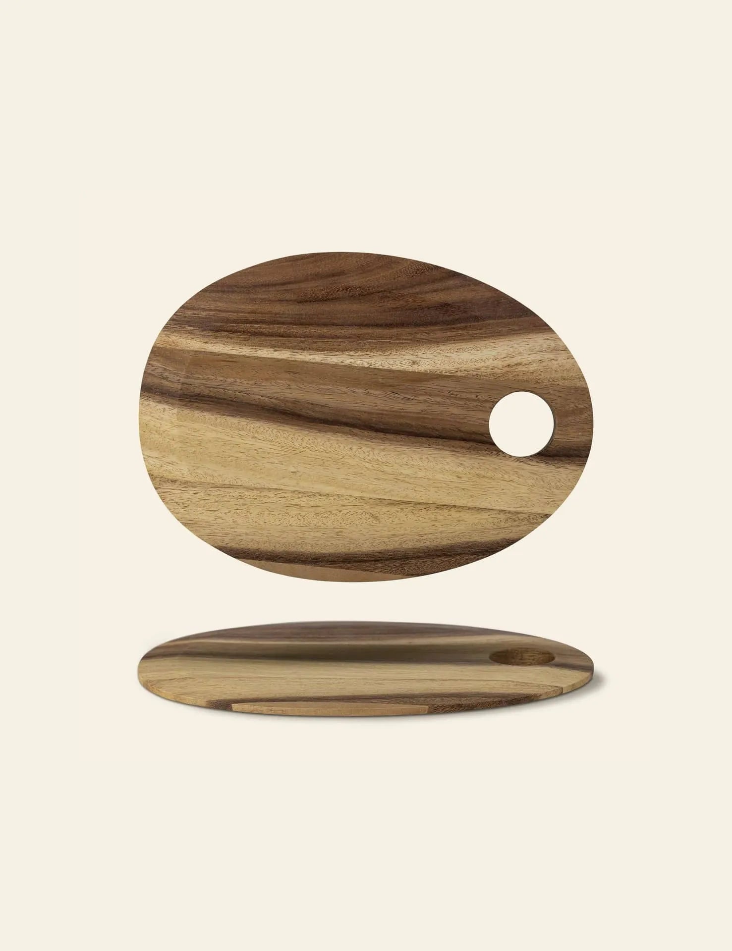 The Bloomingville Guti Cutting Board by Bloomingville is an oval suar wood board with natural grain patterns and a circular hole, shown from top and side views on a plain background—a stylish kitchen accessory.