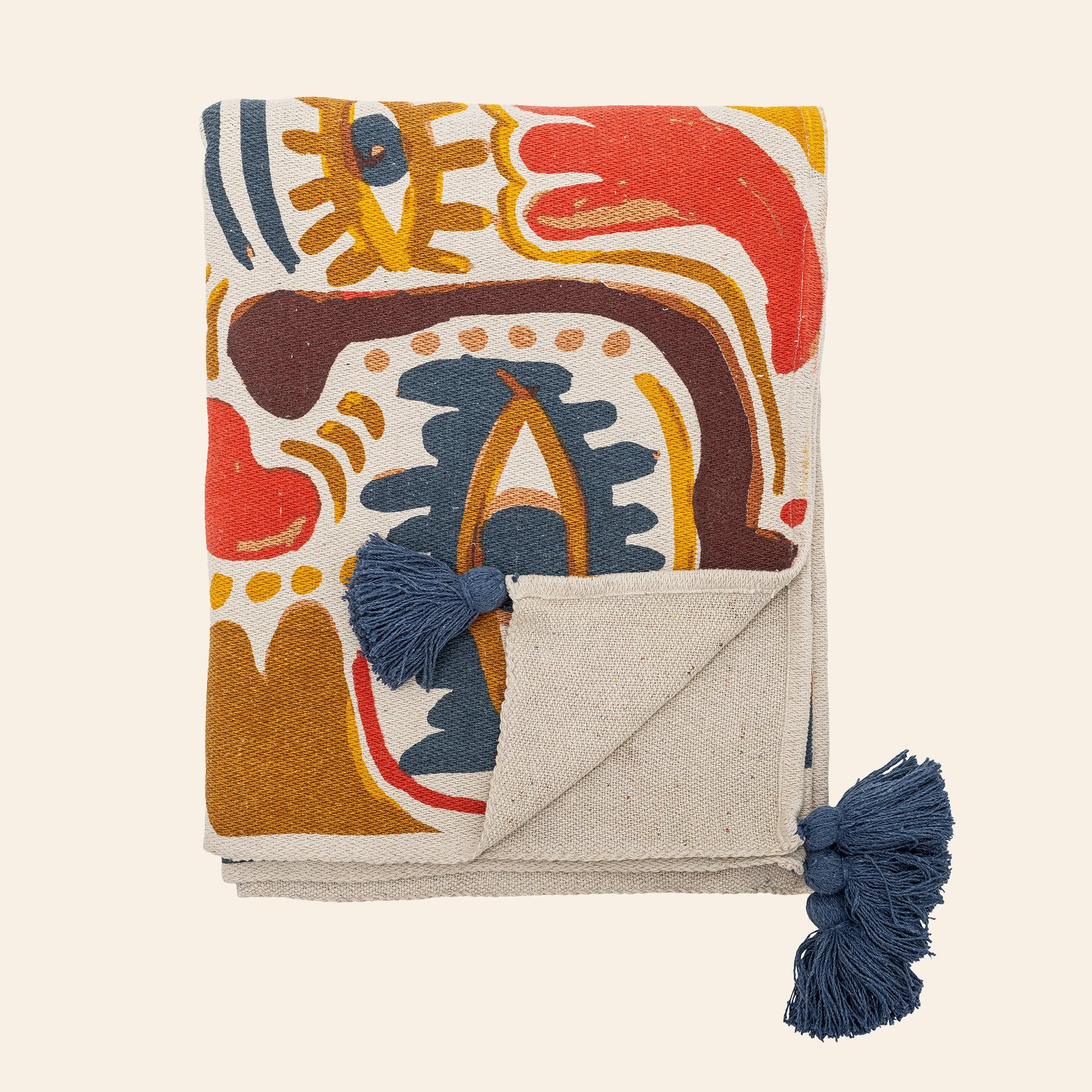 The Bloomingville Horus Throw is a folded beige blanket by Bloomingville with a colorful abstract pattern in red, yellow, blue, and brown, crafted from recycled cotton and featuring blue tassels on two corners, shown on a light background.