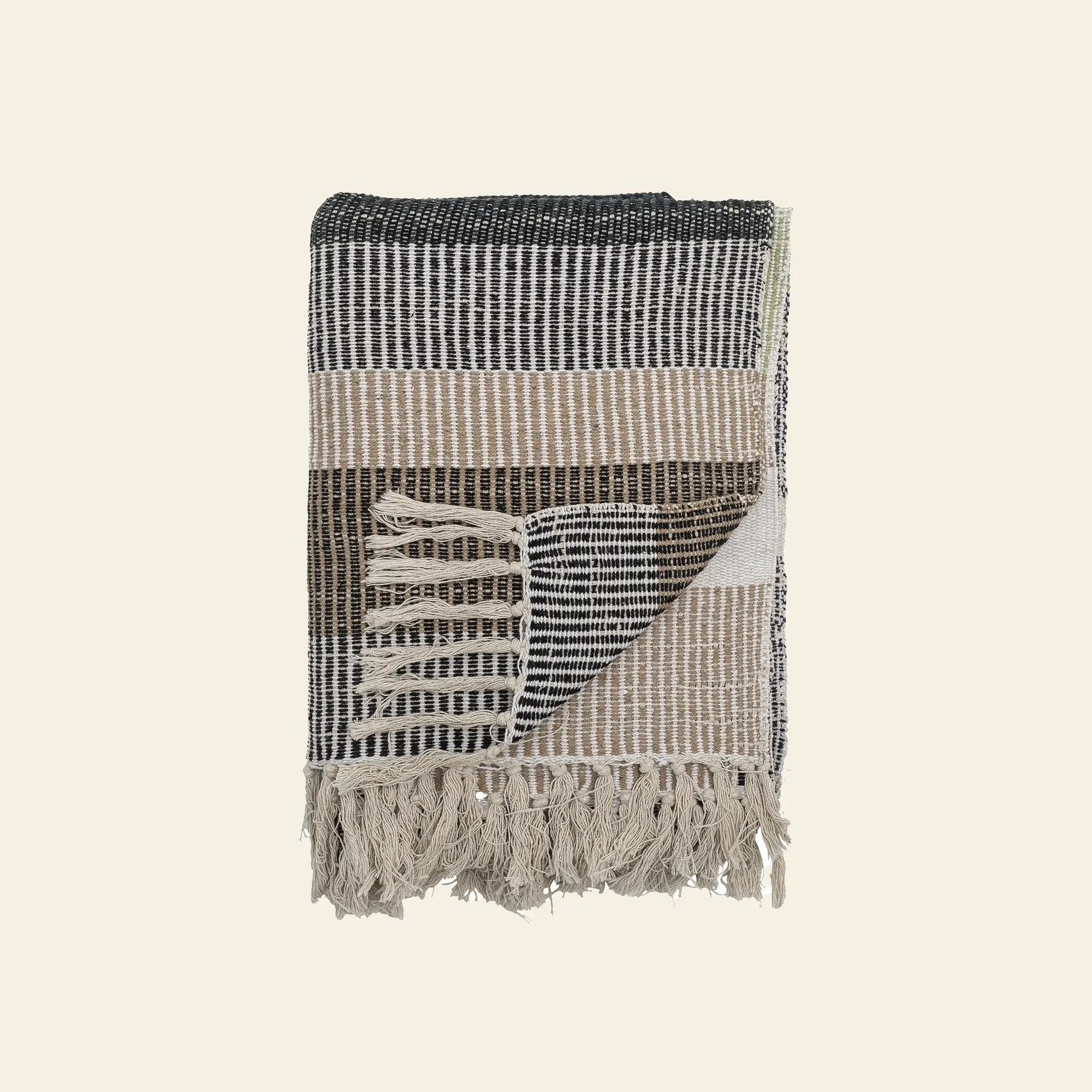 The Bloomingville Isnel Throw, crafted from recycled cotton with black, beige, and white stripes, fringed edges, and a textured pattern, is shown folded against a plain light background.